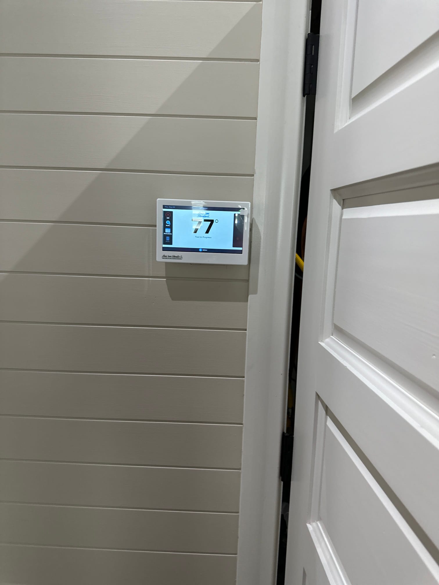 Wall-mounted touchscreen thermostat installed and powered on, displaying an indoor temperature reading of 77 degrees.