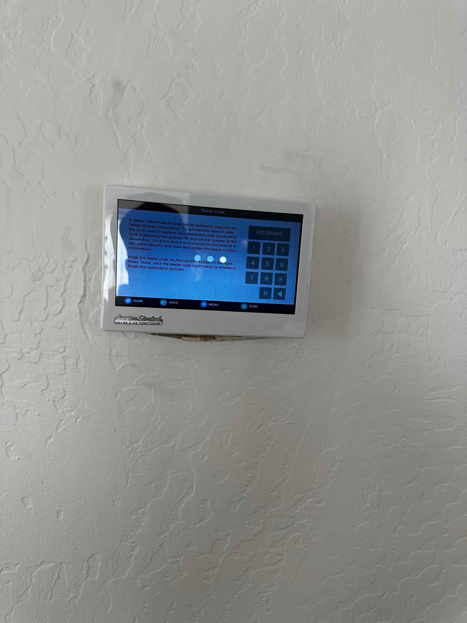 Wall-mounted touchscreen thermostat powered on during setup, displaying dealer code entry and on-screen numeric keypad.