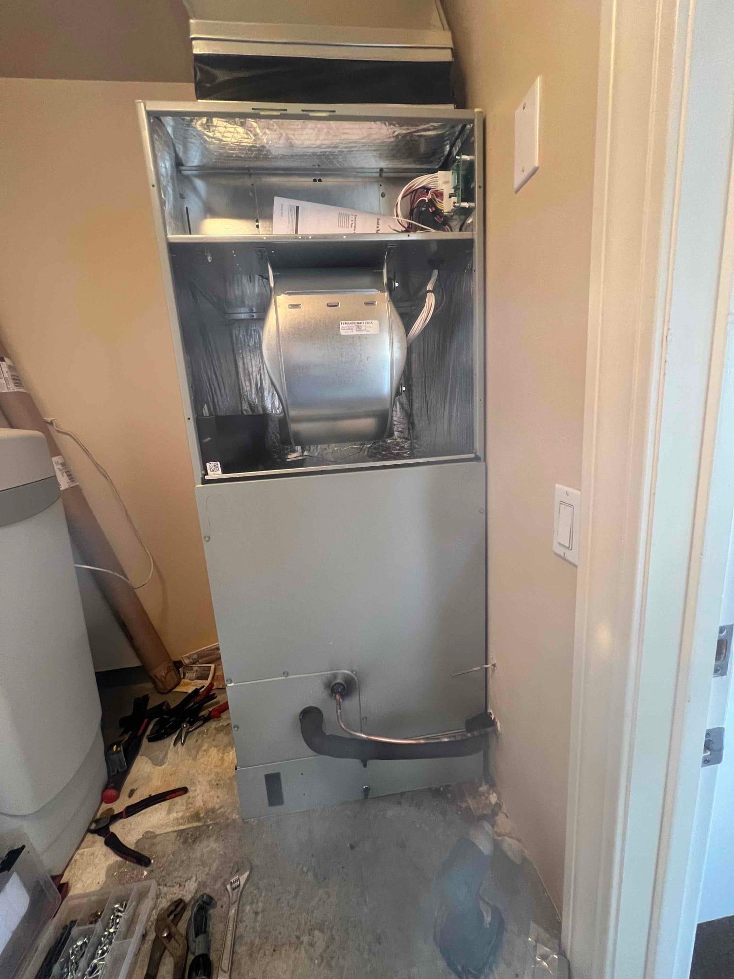 Air handler cabinet installed with blower assembly exposed, new supply plenum, refrigerant line and condensate drain routed, and wiring staged for completion.