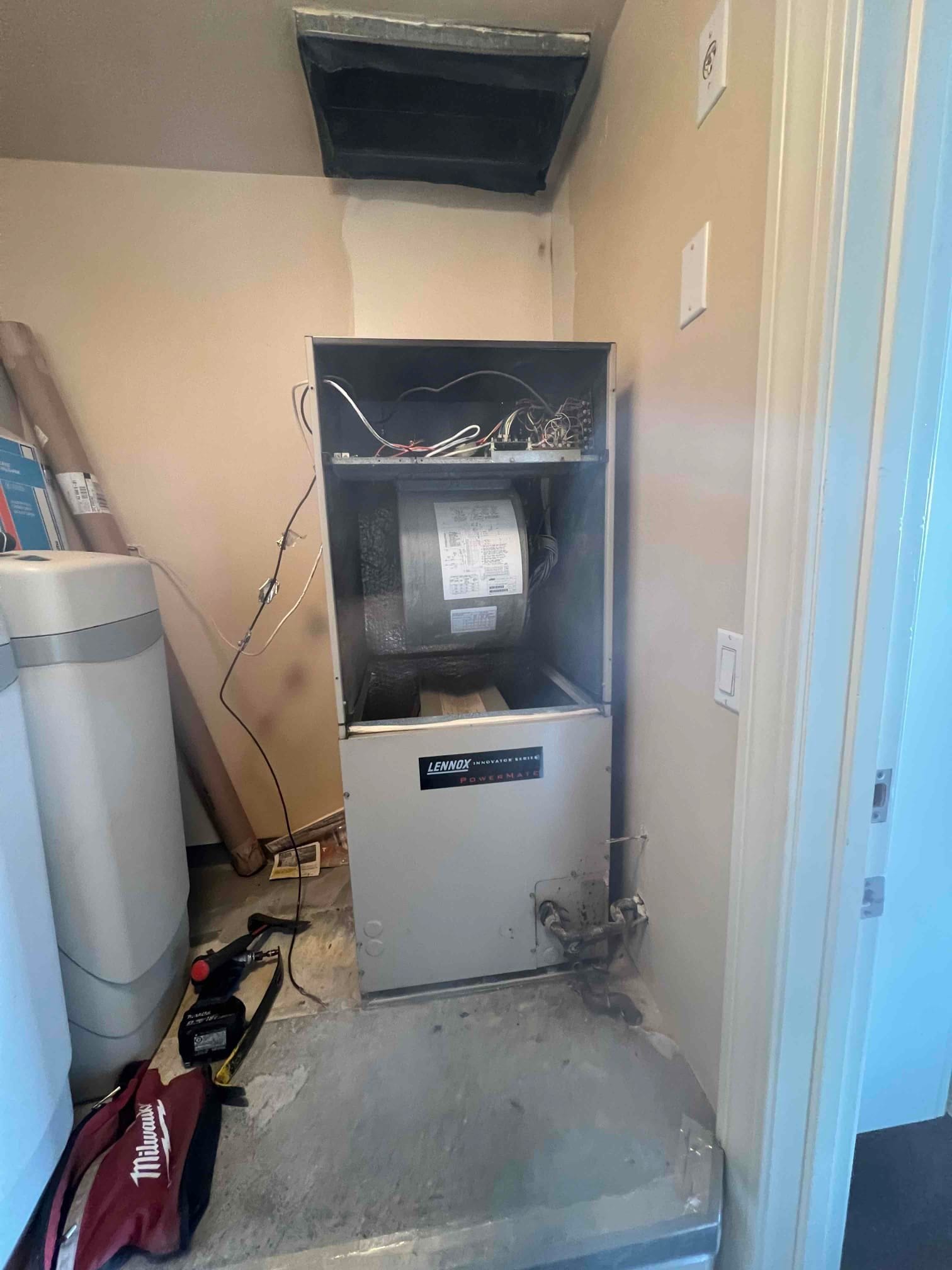 Air handler cabinet open during installation, showing blower assembly, control wiring, return opening above, and condensate drain connection.