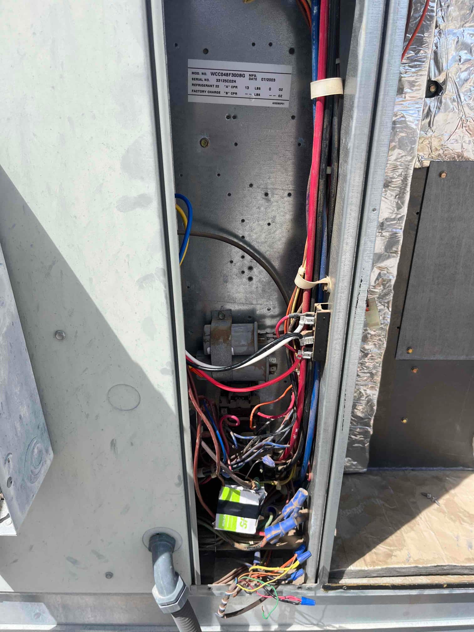 Air handler control compartment open, showing contactor, control board, and wiring harness with conduit connection and insulation panel.
