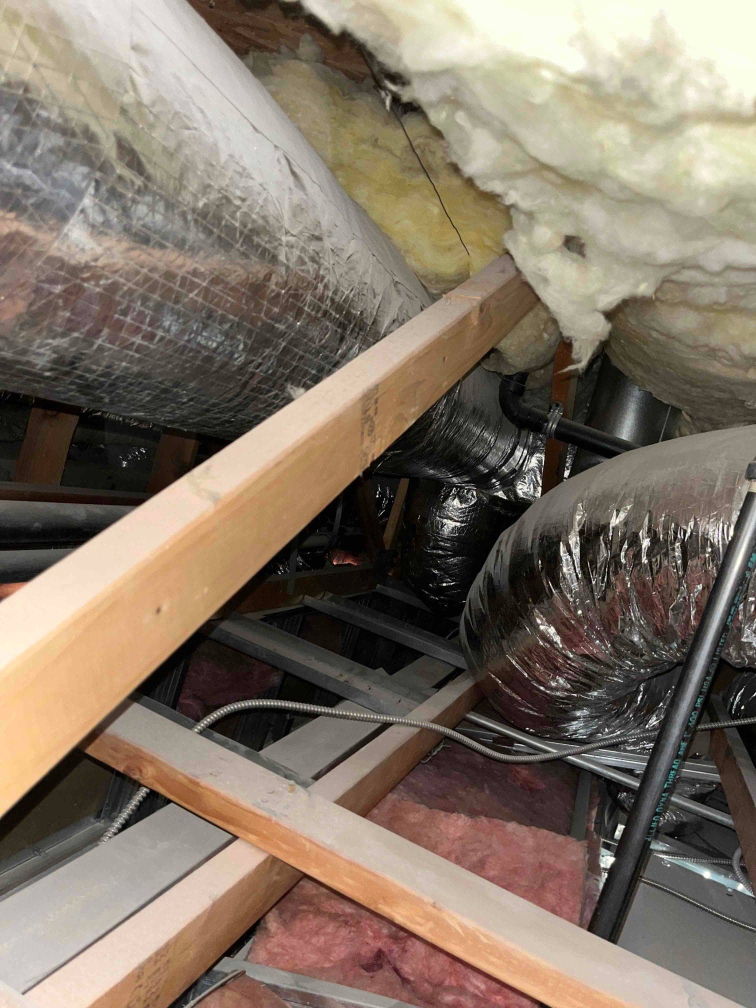 Attic ductwork with flexible insulated air ducts, exposed framing, and fiberglass insulation surrounding the air distribution pathways.