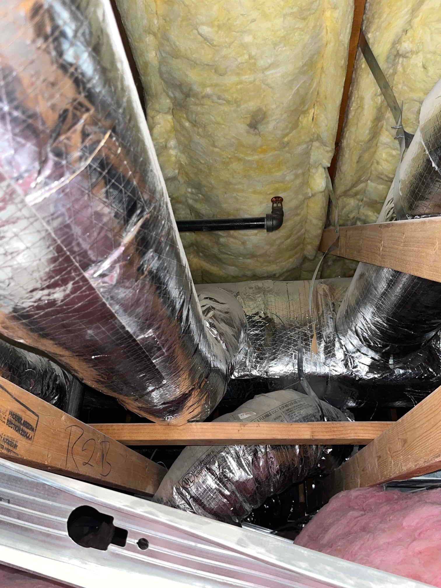 Attic view shows multiple insulated flexible ducts routed between joists with surrounding fiberglass batt insulation.