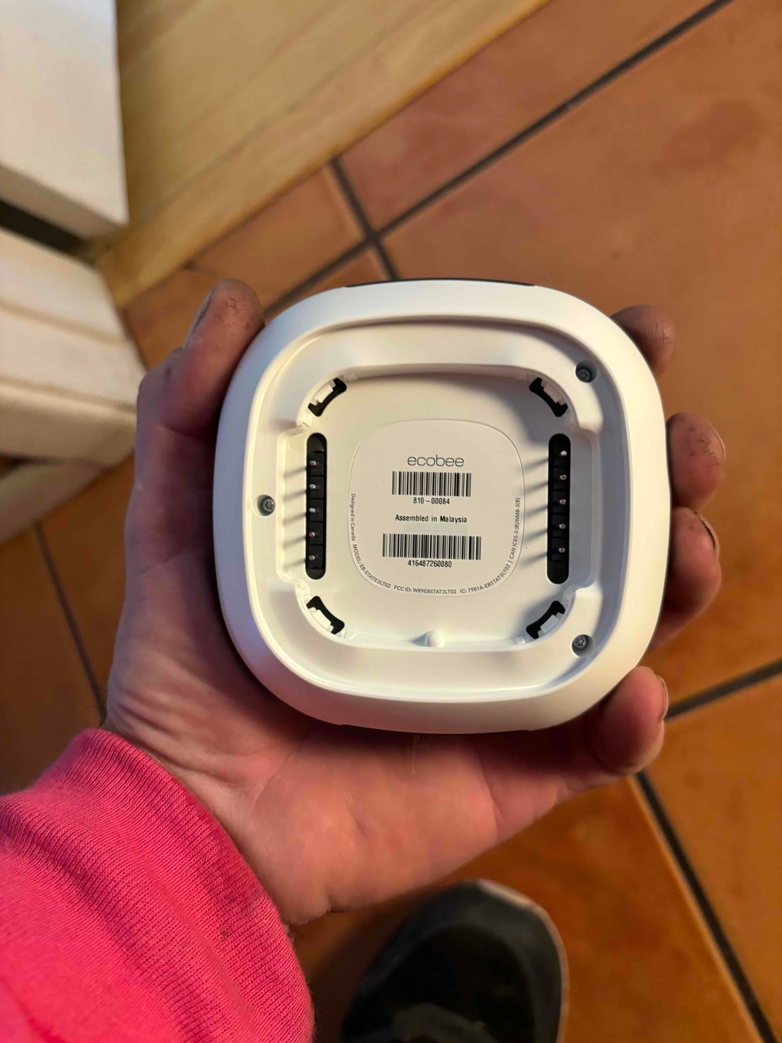 Back of a smart thermostat held during installation, showing terminal blocks and mounting points before wiring to the HVAC system.