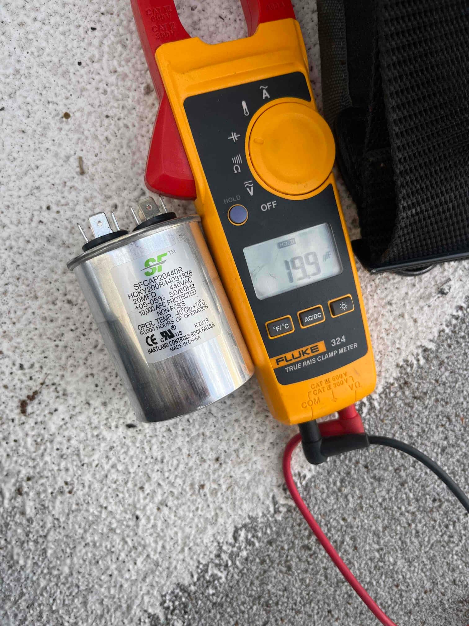Clamp meter display shows 199.9 V while testing near a dual-run capacitor rated 45/5 μF.