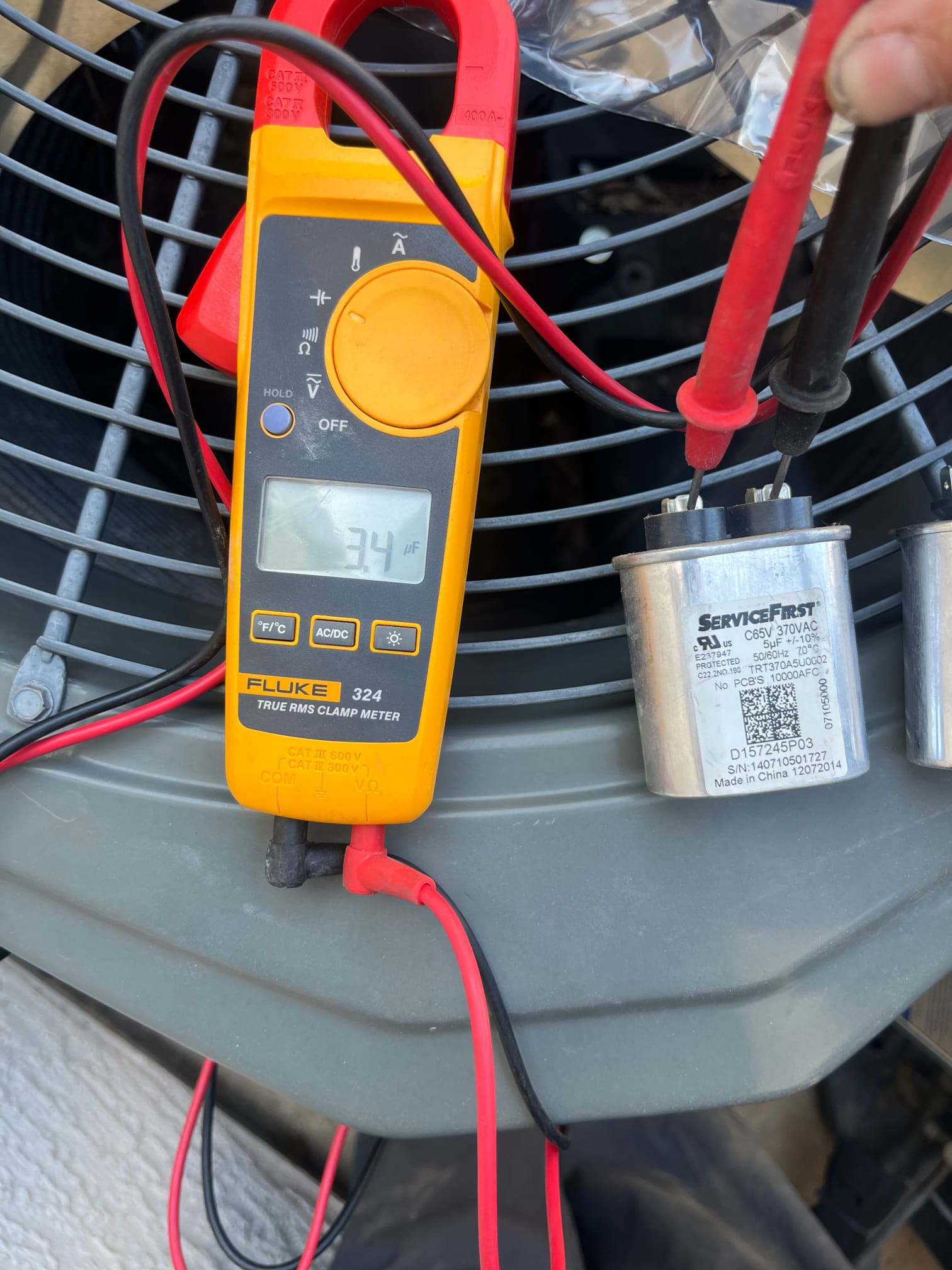 Clamp meter measures 34 µF on the dual-run capacitor using test leads next to the outdoor condenser.