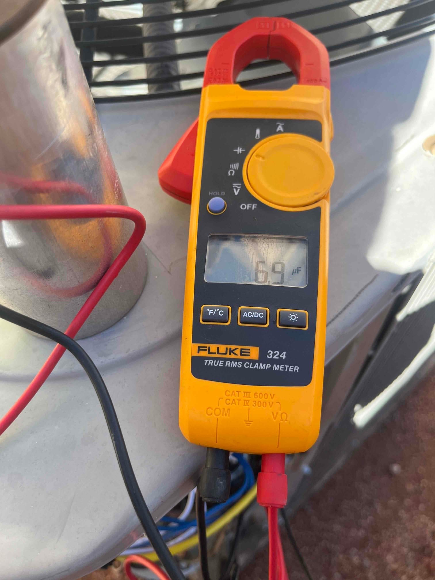 Clamp meter set to capacitance measures 6.9 µF on the connected capacitor leads beside the outdoor condenser.
