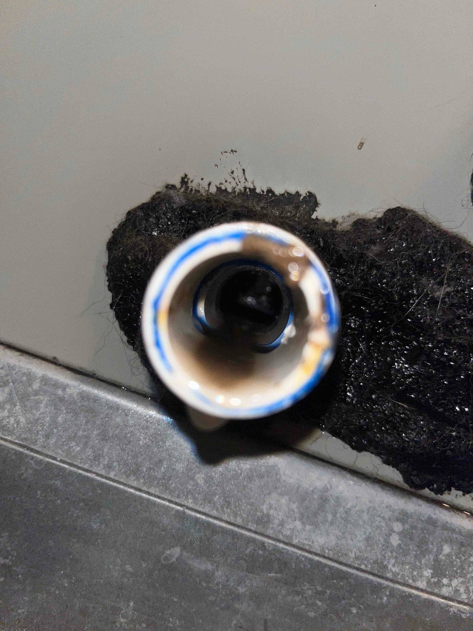 Clogged condensate drain line opening with dark sludge buildup and debris removed from an air handler pan.