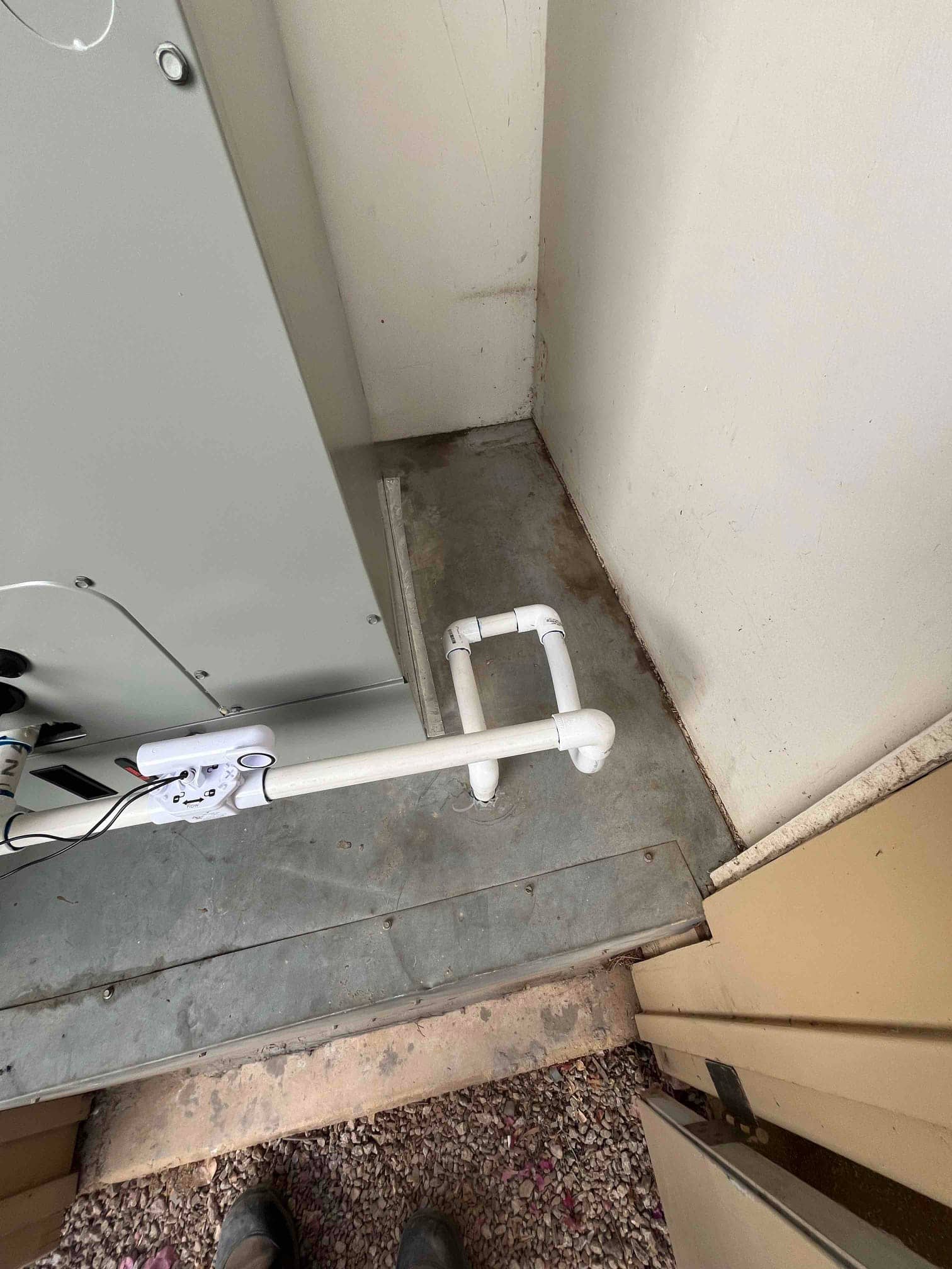 Condensate drain assembly with float switch installed at an air handler on a metal platform in a utility closet.