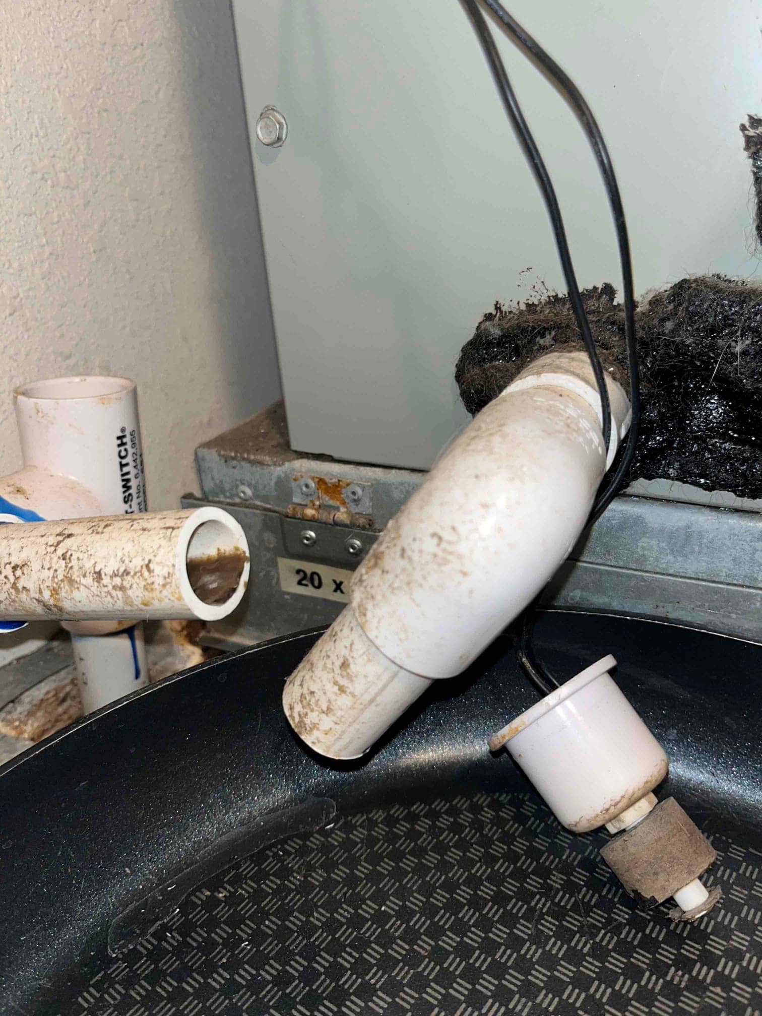 Condensate drain assembly with inline float switch hanging above a drain pan near the air handler cabinet.