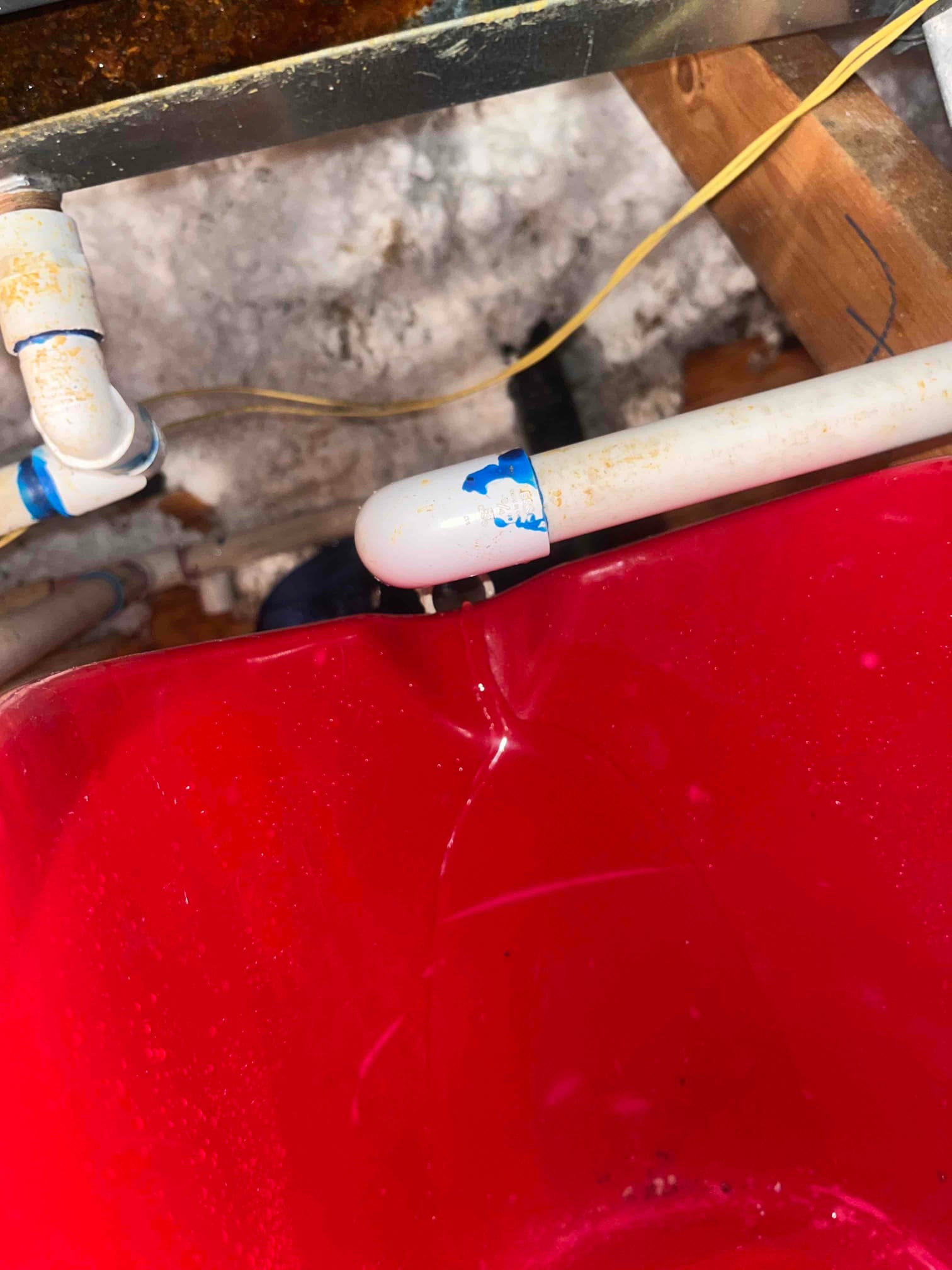 Condensate drain line discharging into a red bucket, showing water dripping from the PVC elbow under the air handler.