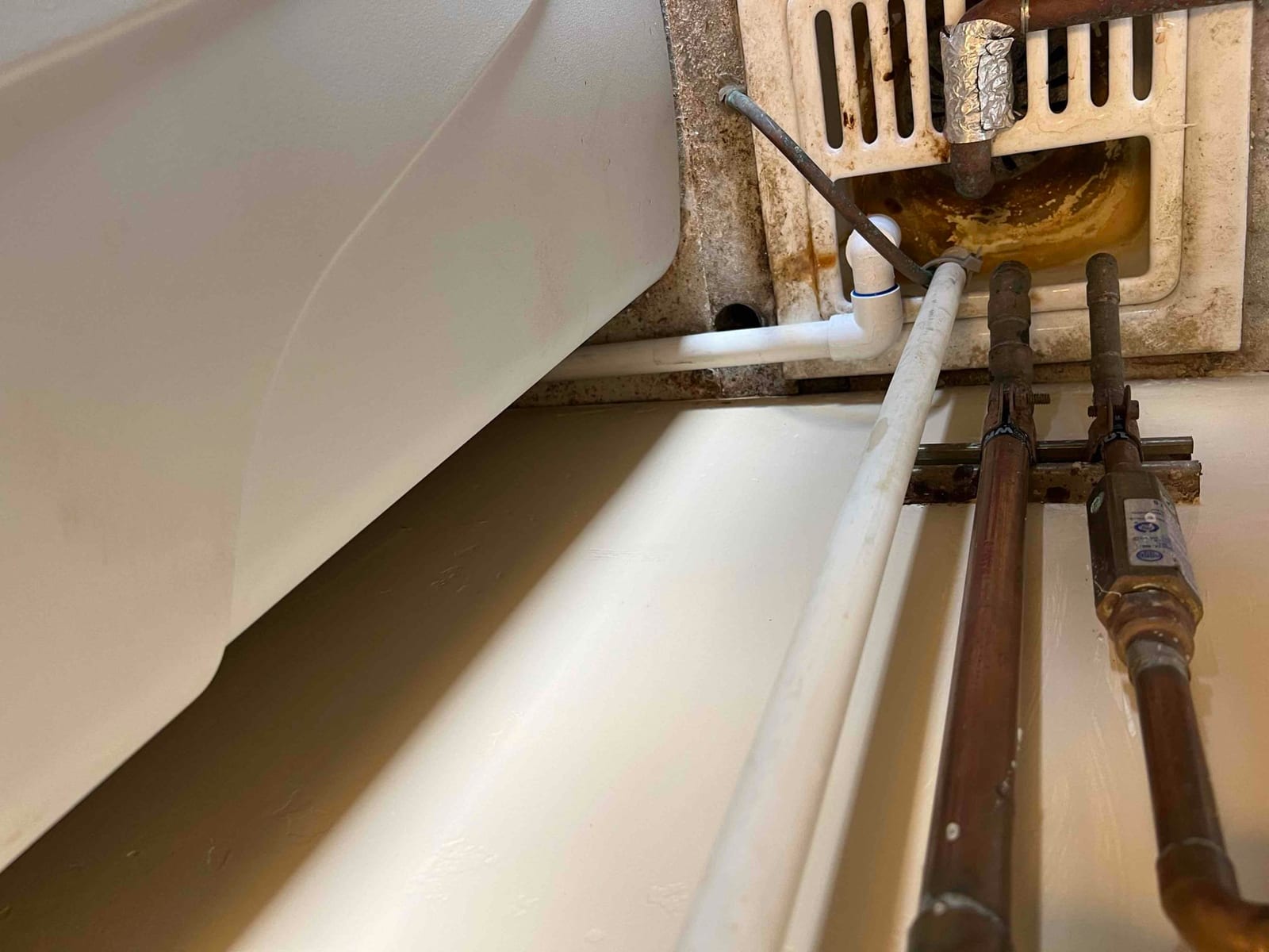 Condensate drain piping and copper refrigerant lines routed to a floor drain pan beneath the indoor unit.