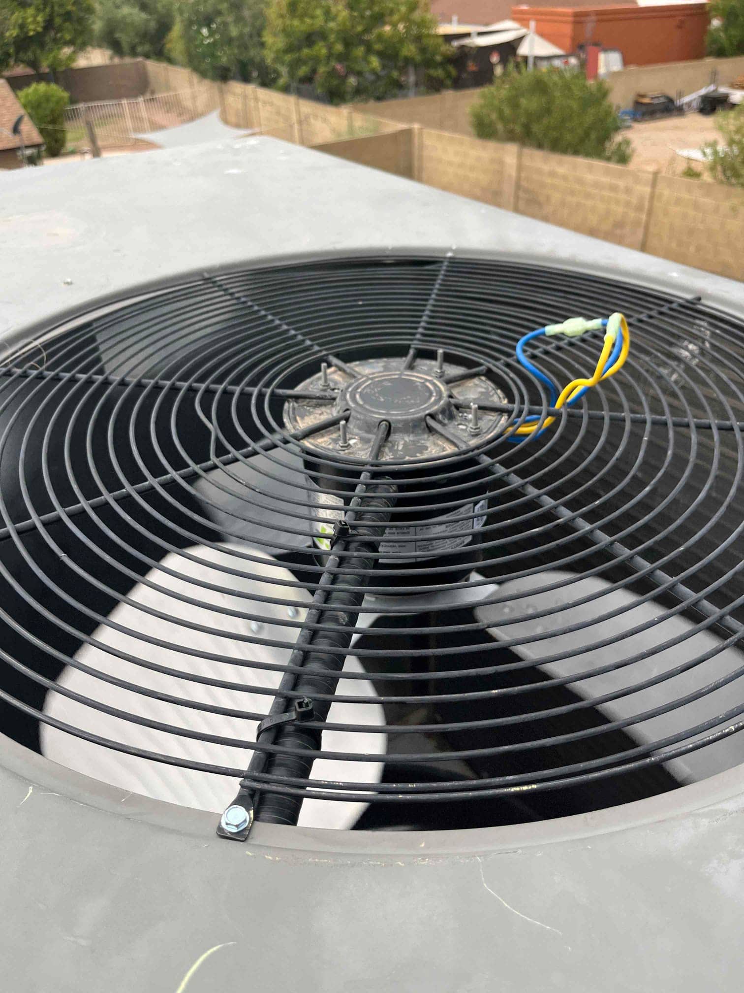 Condenser fan assembly on rooftop unit, showing fan guard, hub, and connected motor wiring with wire nuts.