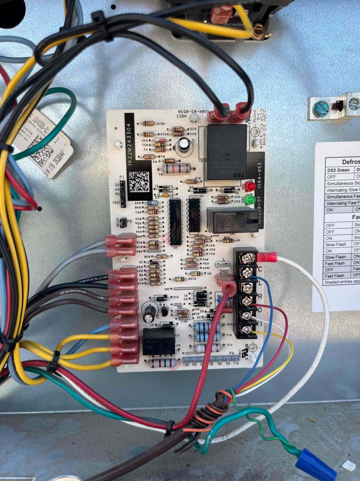 Control board inside the outdoor condenser compartment with connected low-voltage and high-voltage wiring and labeled terminal strip.