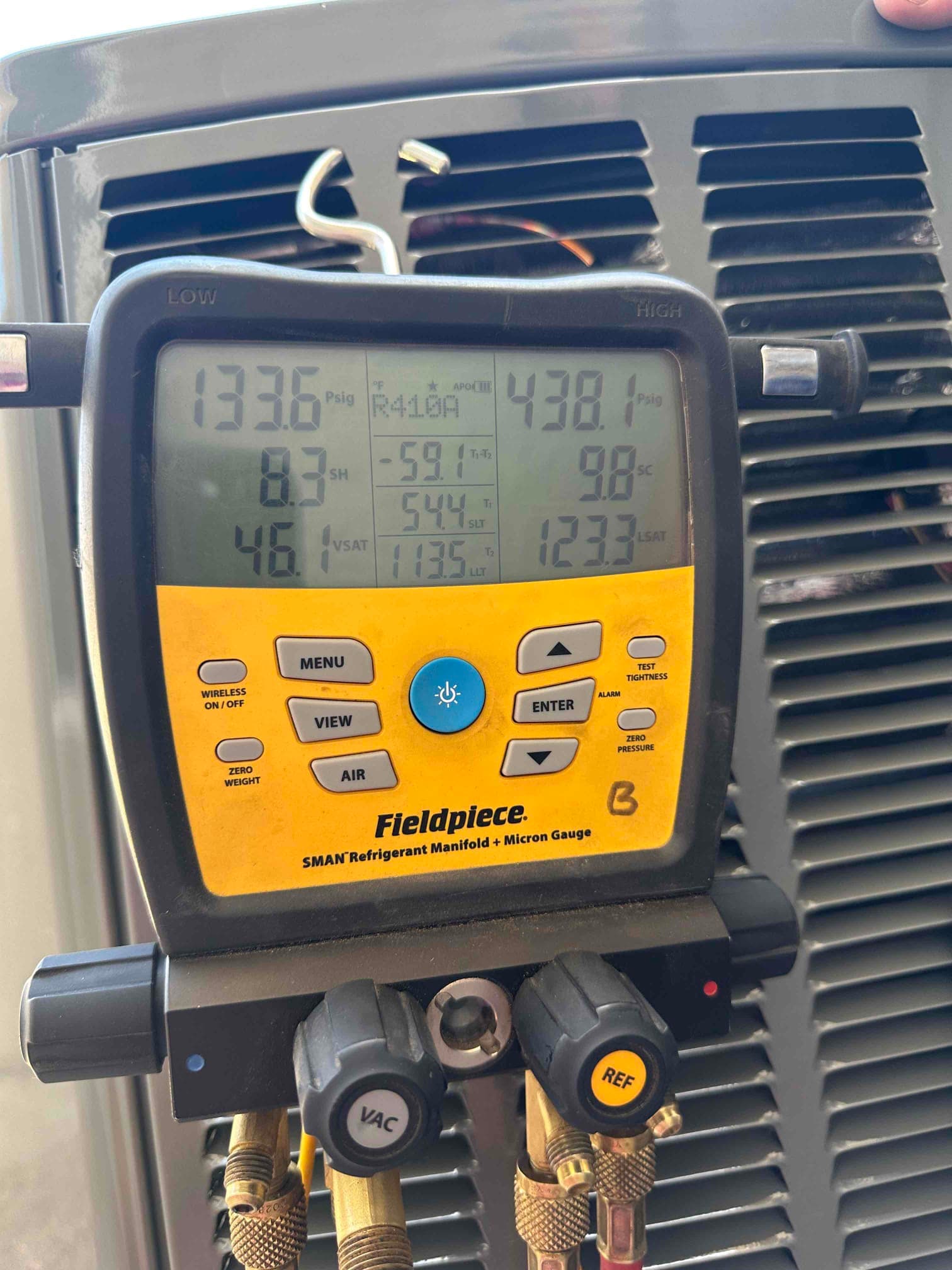 Digital manifold connected at the outdoor unit shows operating pressures and calculated superheat and subcooling during system checkout.
