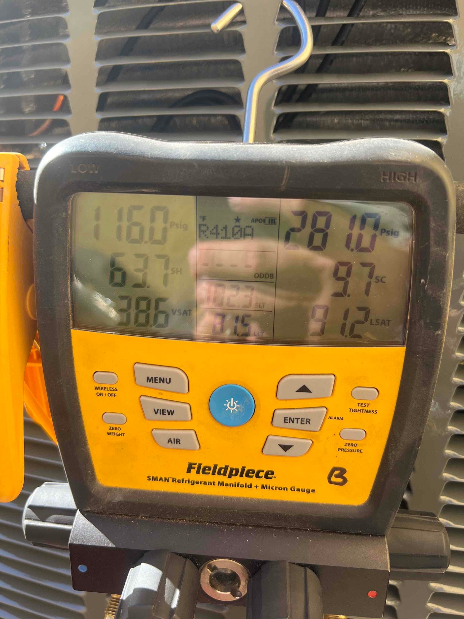 Digital manifold connected at the outdoor unit shows operating pressures and calculated subcooling and superheat during system commissioning.