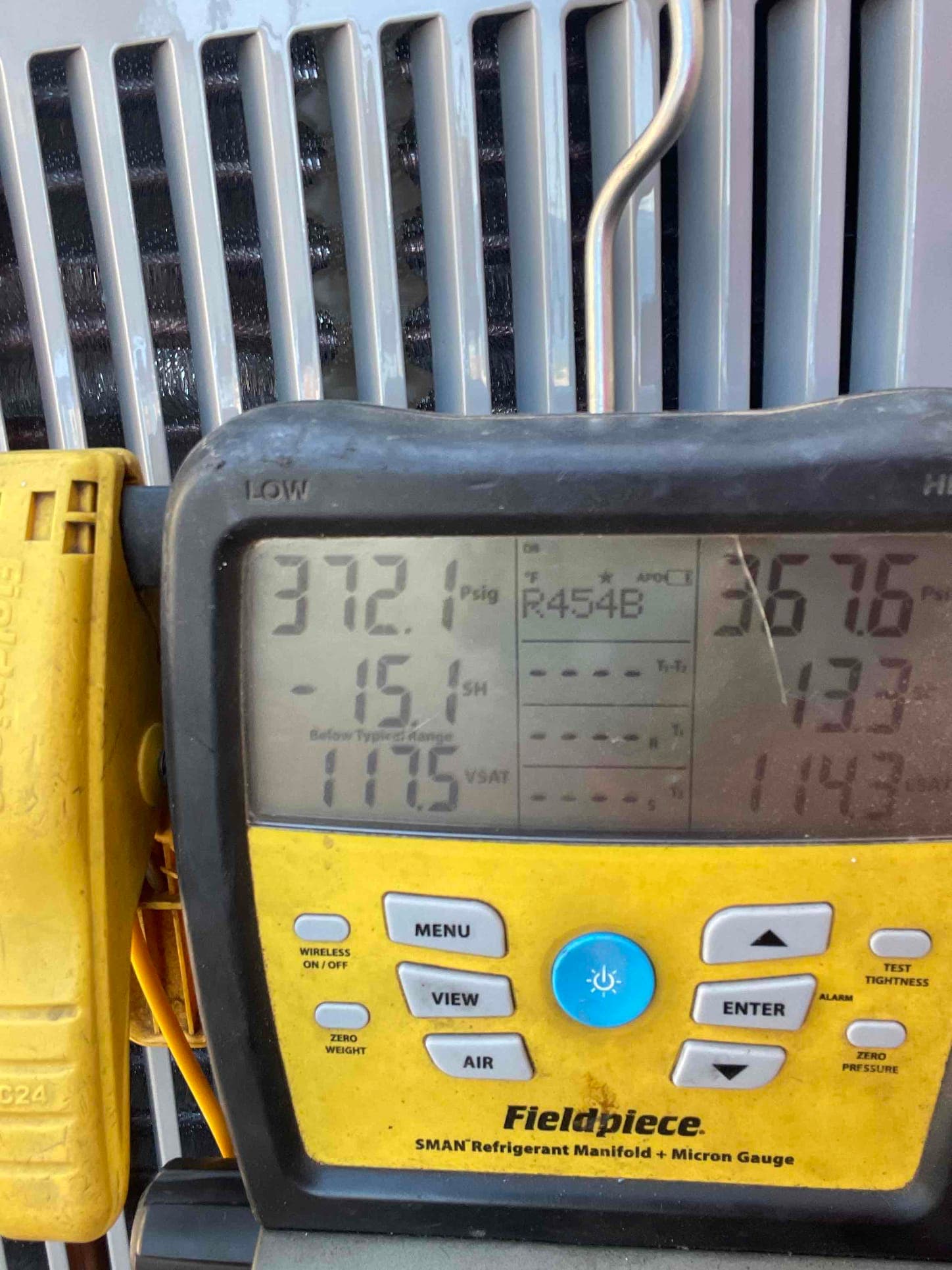 Digital manifold gauge on the condenser shows operating pressures while charging and commissioning a new air conditioning system.