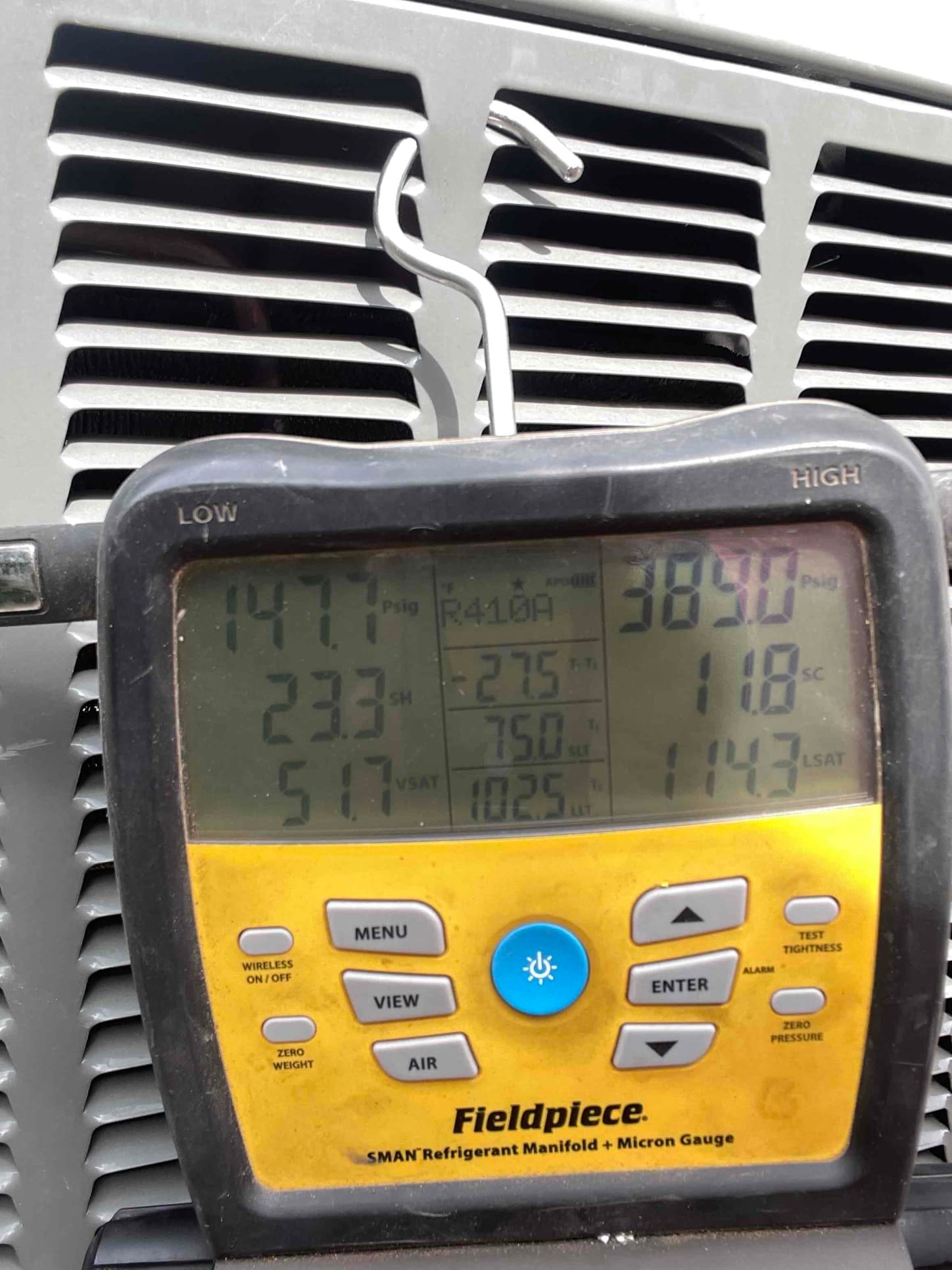 Digital manifold gauge on an outdoor condenser shows 147.1 psi high-side pressure and 38.8 psi low-side pressure with R-410A selected.