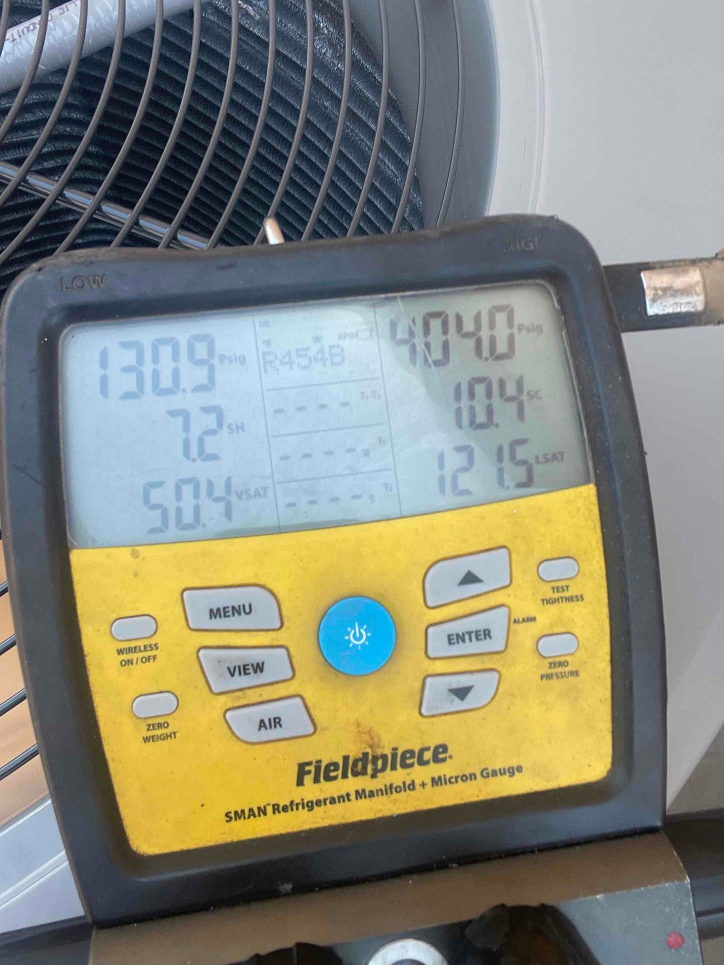 Digital manifold on the outdoor unit shows operating pressures and readings during system commissioning with refrigerant flowing.