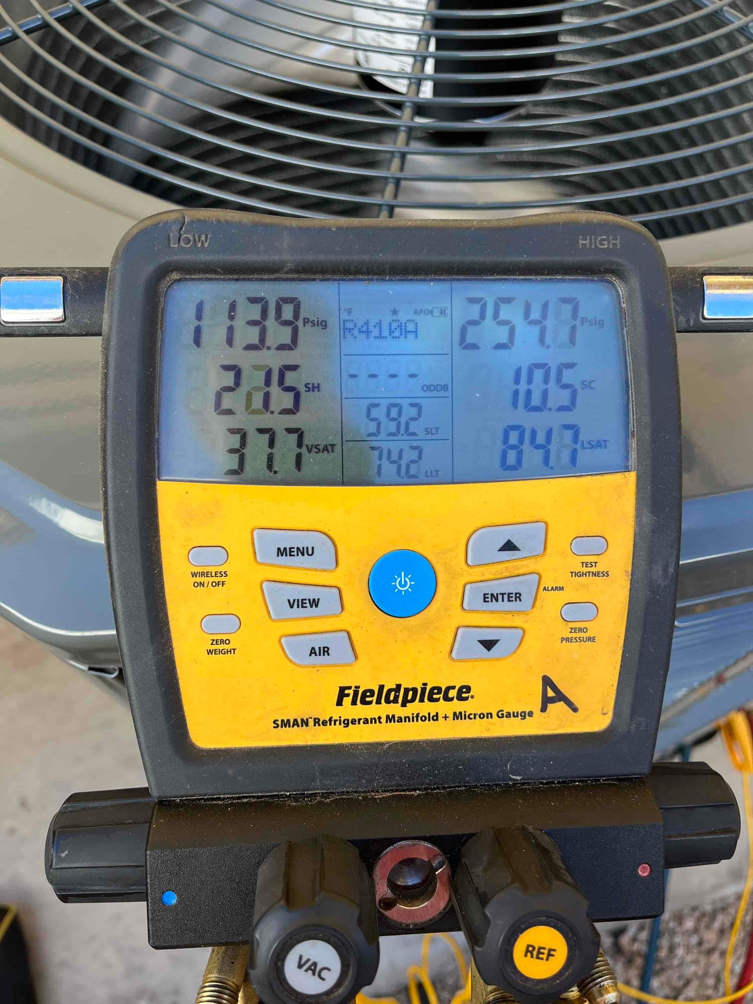Digital manifold shows system operating pressures with superheat and subcooling while the outdoor unit runs during commissioning.