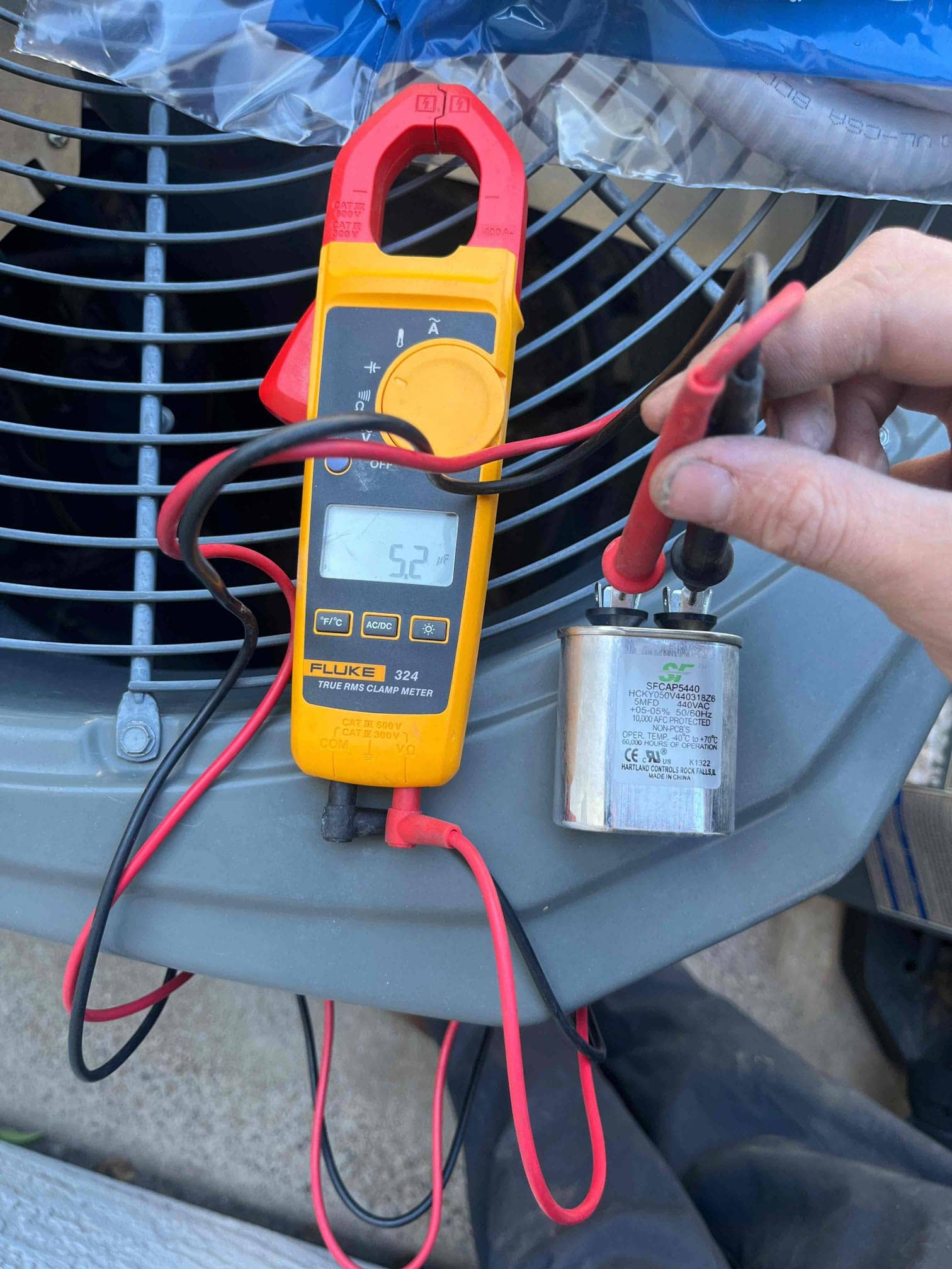 Digital multimeter measures 52.1 μF on the dual-run capacitor while leads are connected across its terminals.