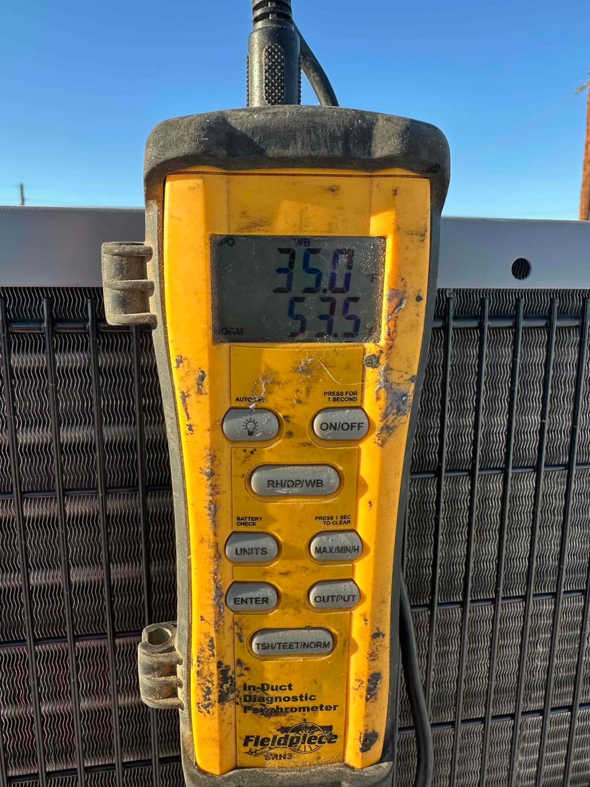 Digital psychrometer measures in-duct air temperatures, displaying 35.0 and 57.5 degrees on the screen during airflow commissioning.