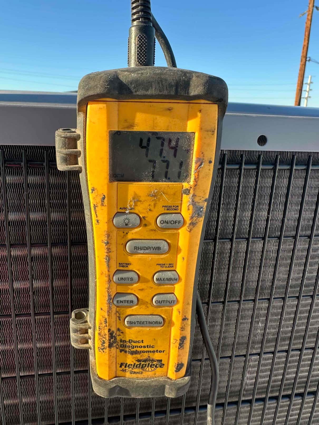 Digital psychrometer shows air temperature of 77.1 degrees during airflow and humidity measurements at the outdoor unit.