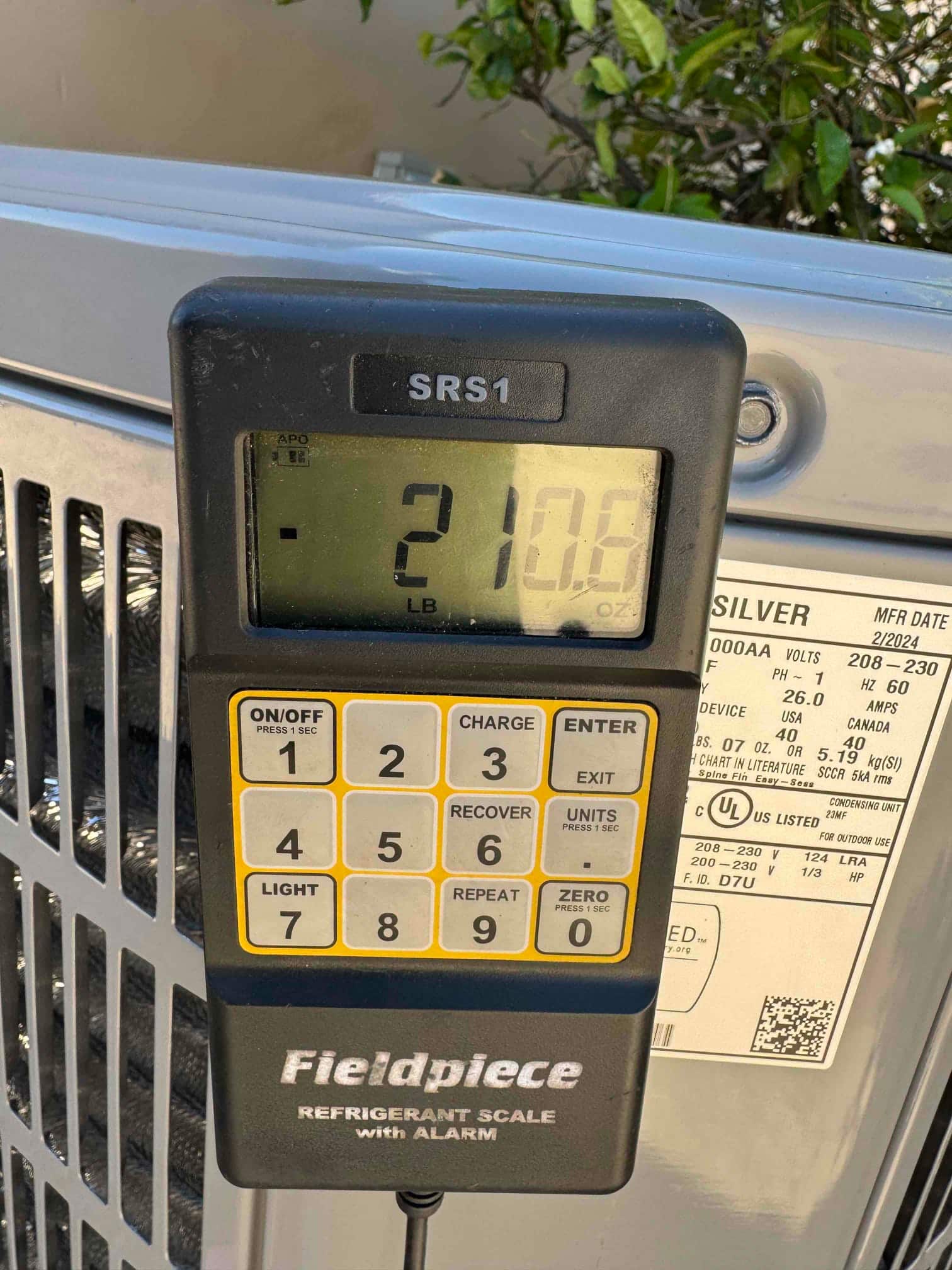 Digital refrigerant charging scale shows 21 pounds 0.6 ounces during commissioning at the outdoor condenser.