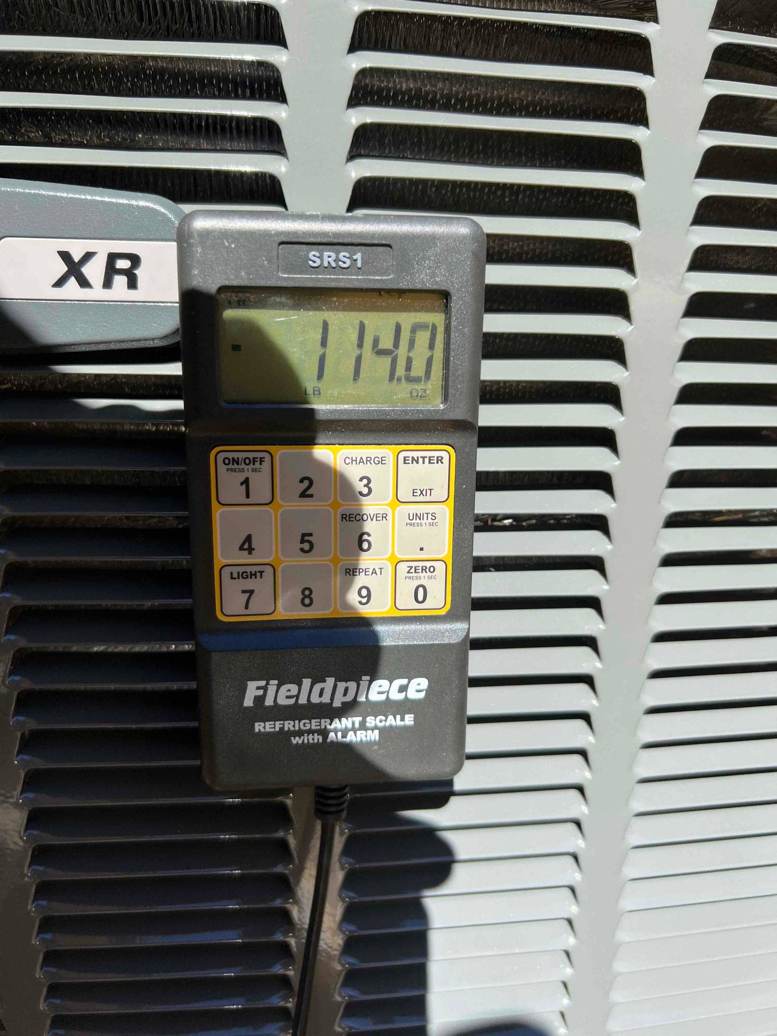Digital refrigerant scale displays 11.40 pounds while positioned against the outdoor condenser cabinet during charging work.