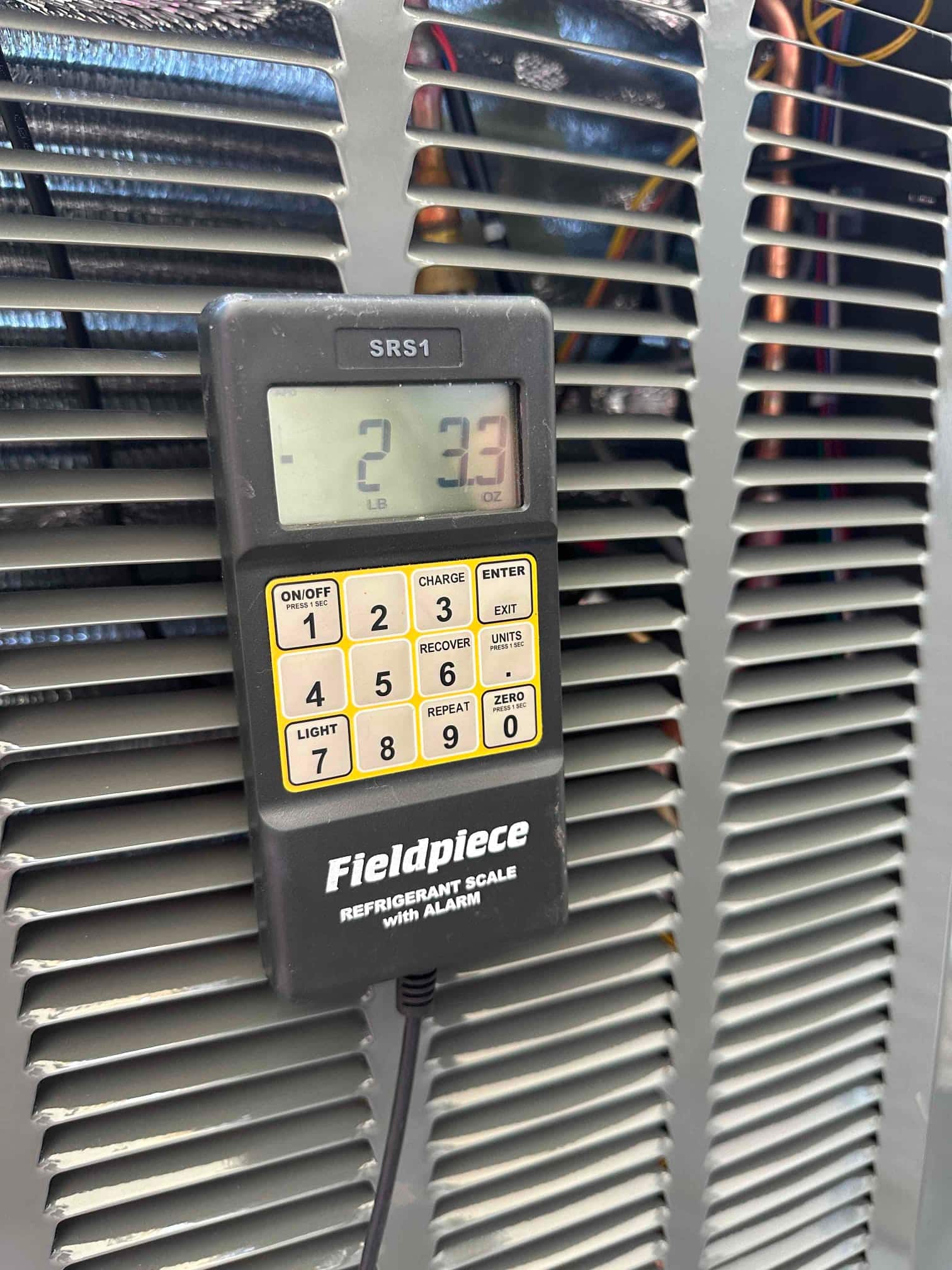 Digital refrigerant scale displays 2 pounds 3.3 ounces during charging while positioned against the outdoor condenser housing.