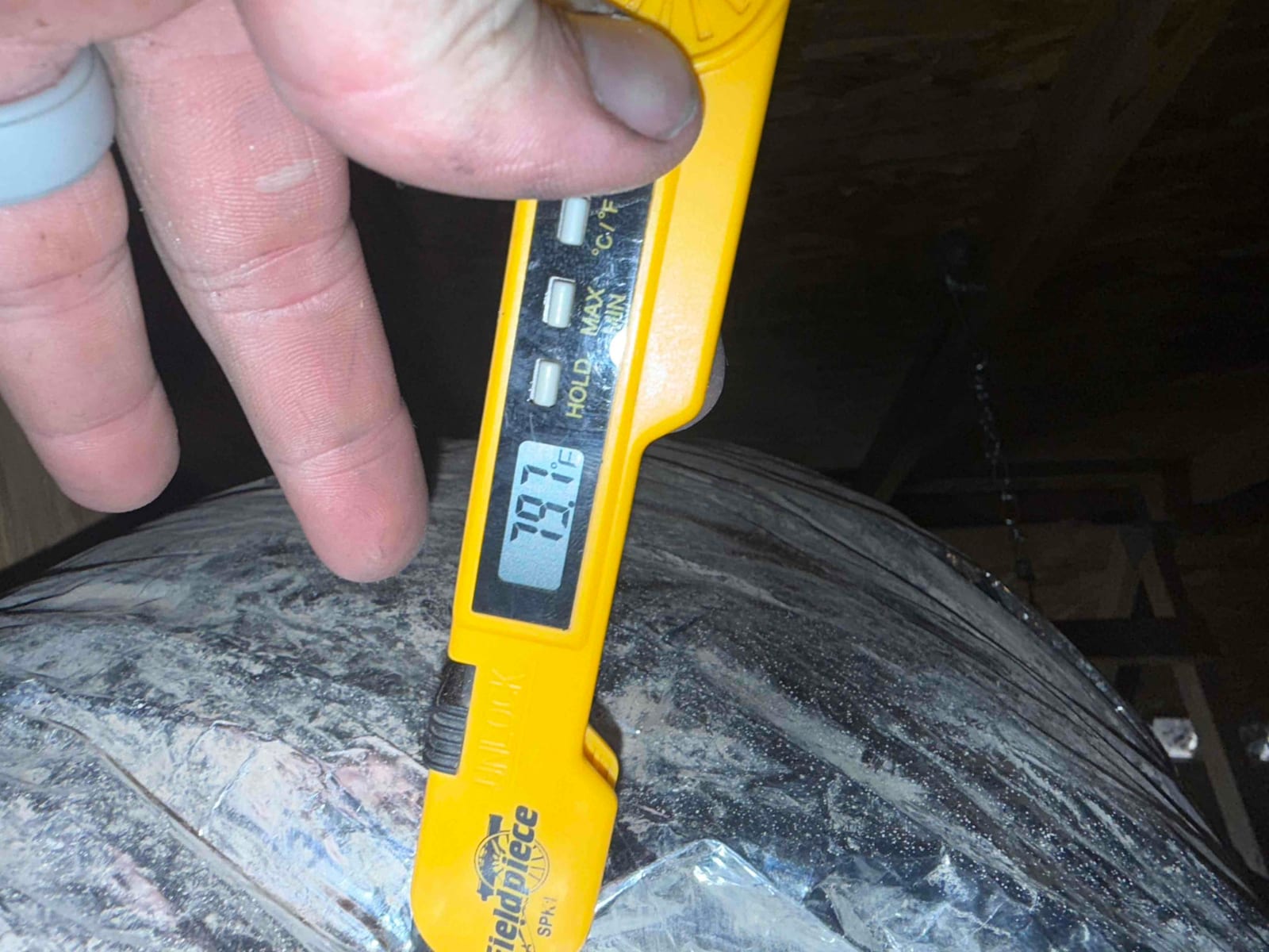 Digital thermometer pressed against insulated duct shows 78.7°F, documenting return air temperature during air-side commissioning.