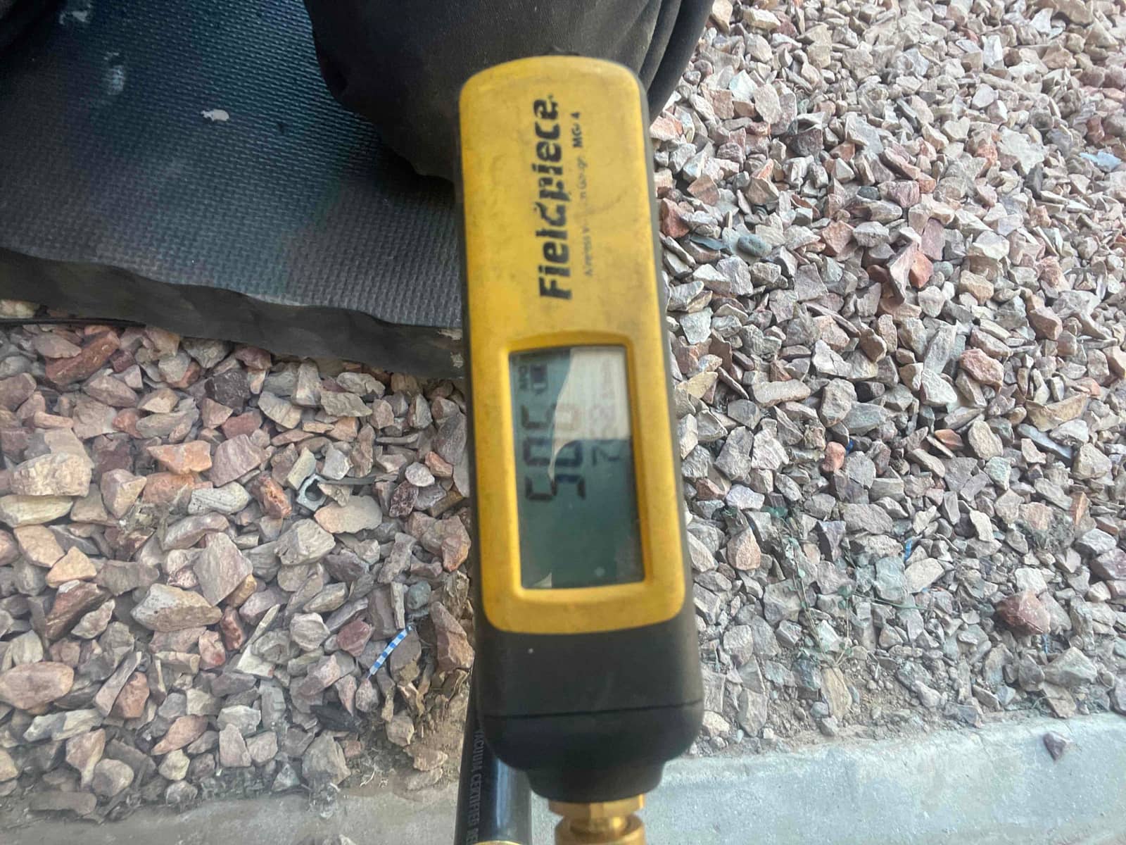 Digital thermometer probe displays 50°F while measuring air temperature during system checkout at the outdoor installation area.