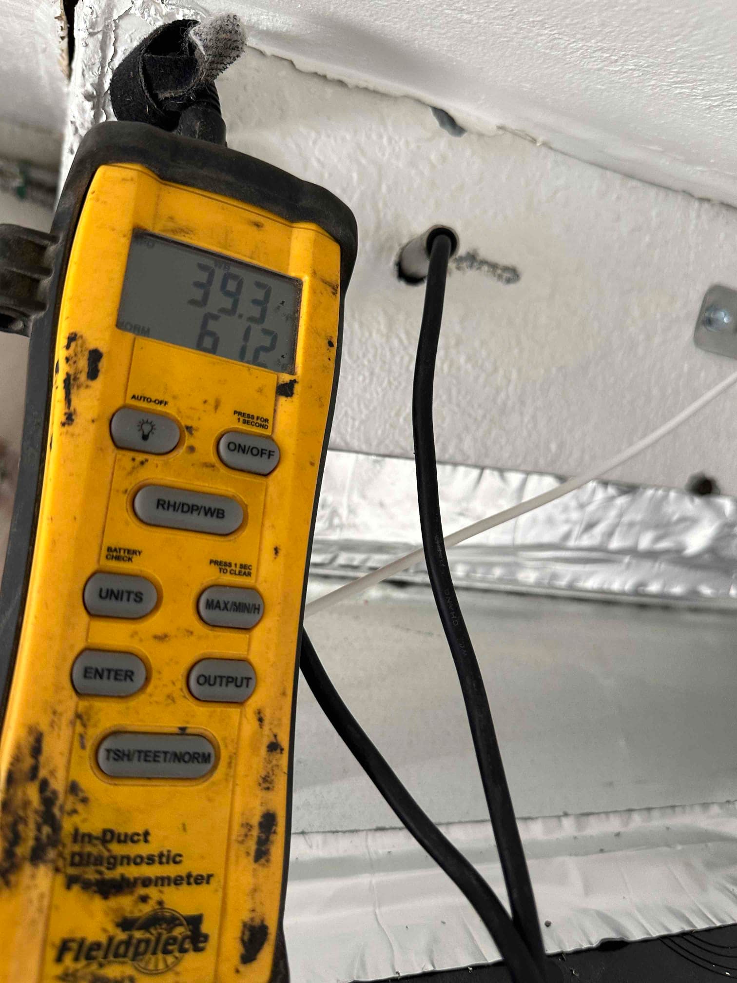 Digital thermometer probe inserted into duct with display reading 39.3 and 61.2, documenting air temperature during commissioning.
