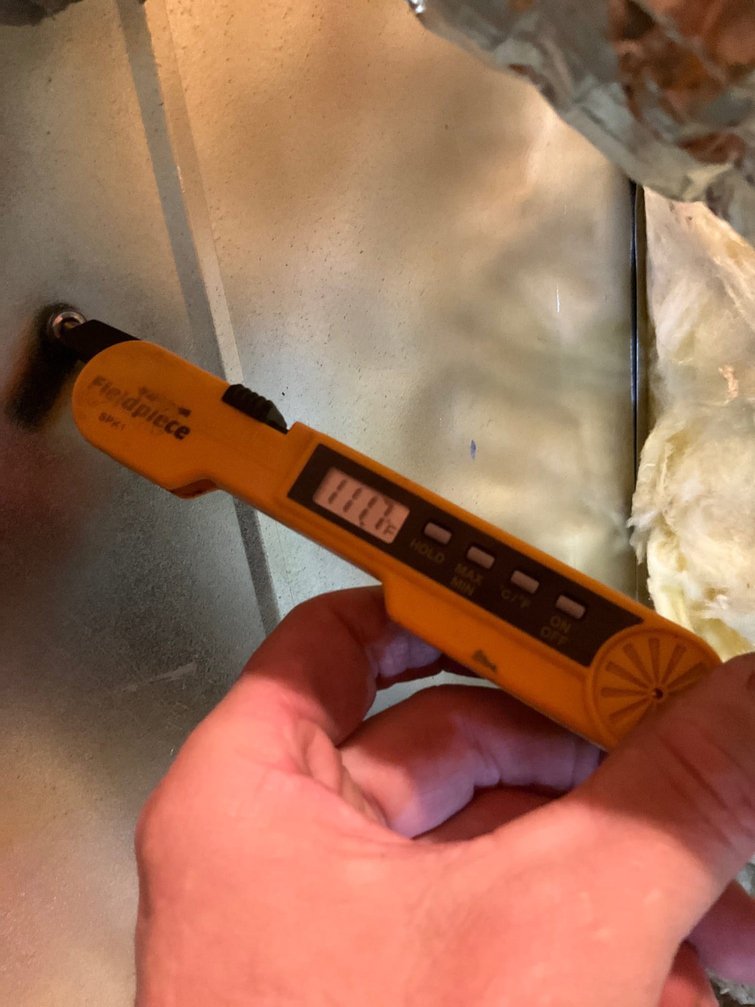 Digital thermometer probe inserted into duct measures air temperature, showing 77.1 degrees on the display during airflow testing.
