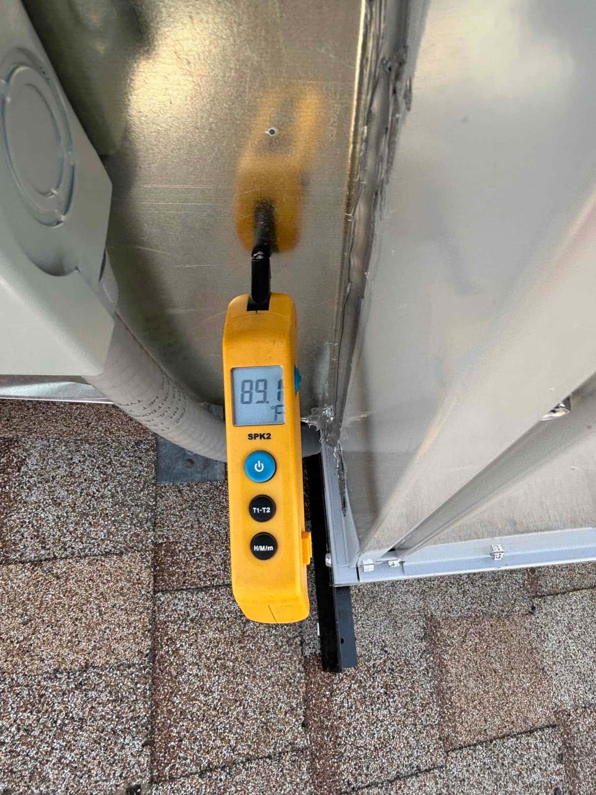 Digital thermometer probe inserted into duct panel reads 89.1°F while checking air temperature during system commissioning.
