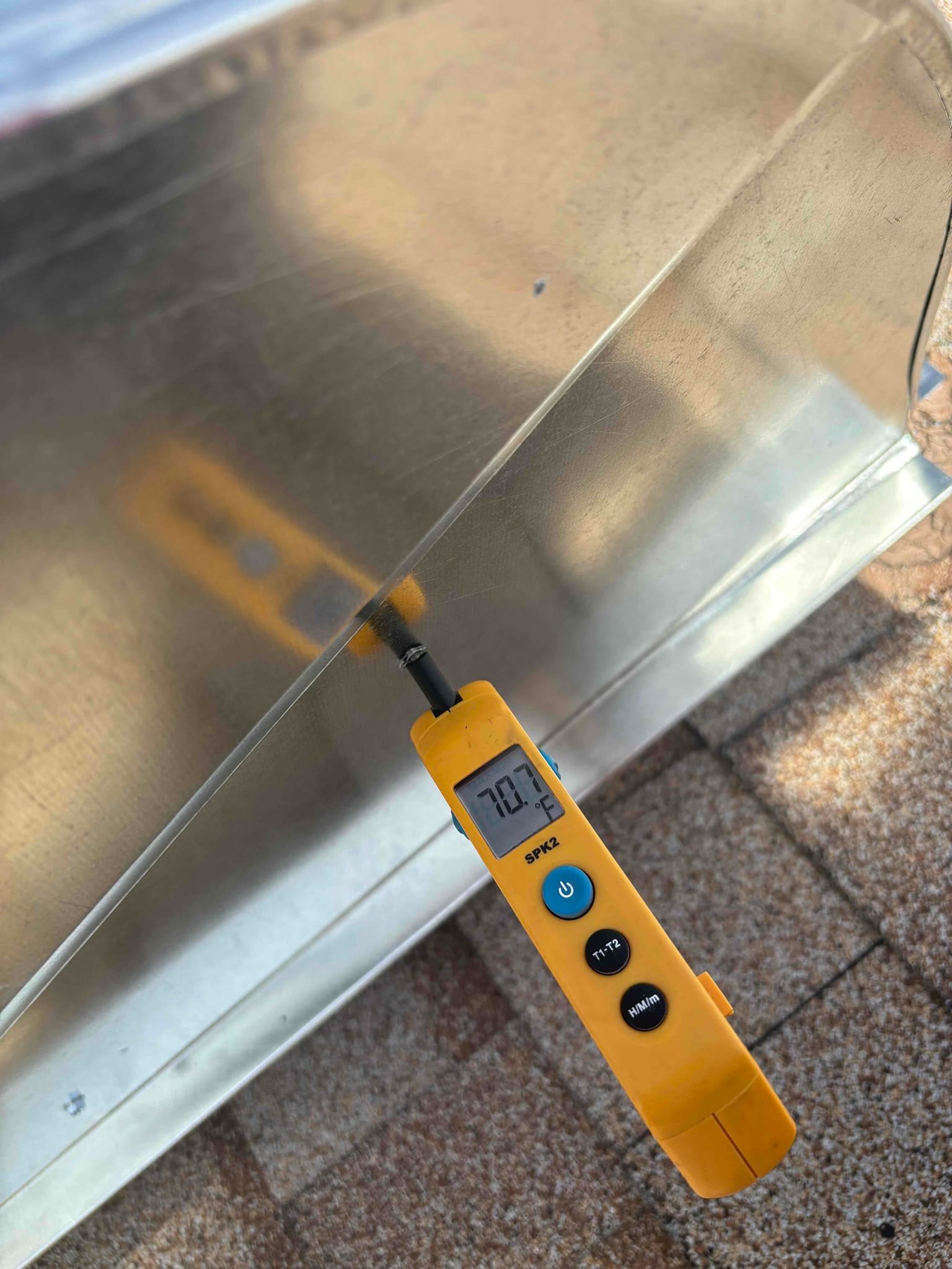 Digital thermometer probe inserted into metal duct reads 70.7°F, documenting return air temperature during commissioning.