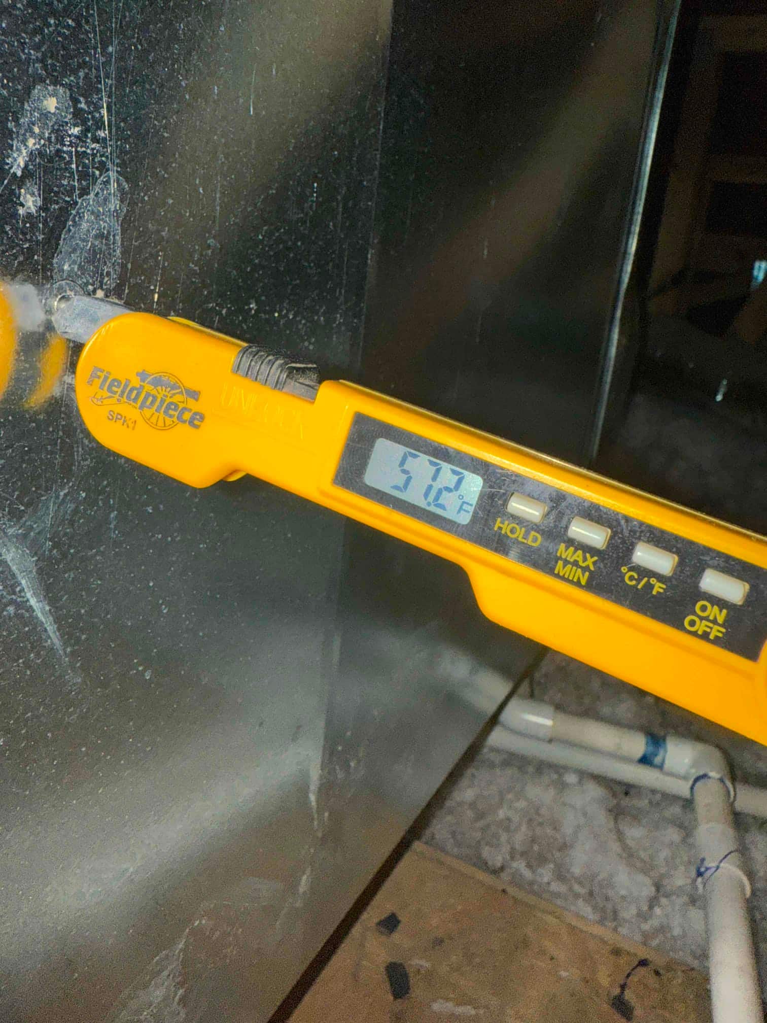 Digital thermometer probe inserted into metal duct shows 57.2°F, documenting cold supply air temperature after the evaporator.