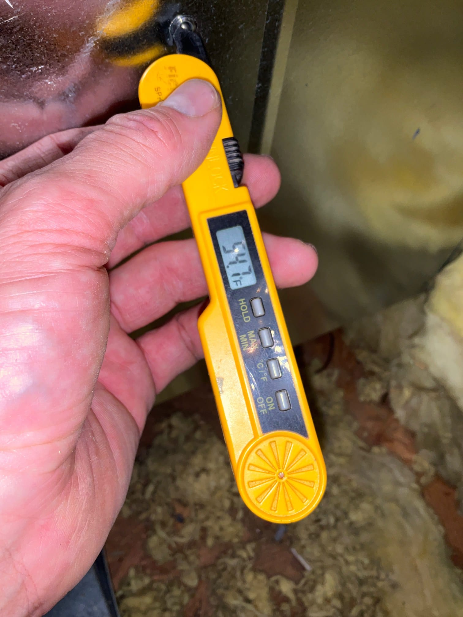 Digital thermometer probe measures supply air temperature at the duct, displaying 54.4°F during system commissioning.