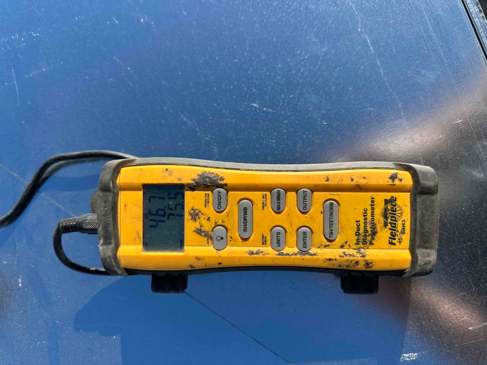 Digital thermometer shows duct air temperature during commissioning to verify cooling performance.