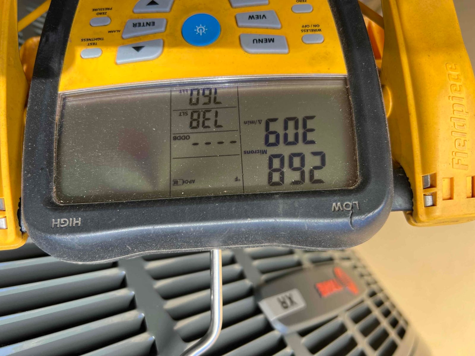 Digital vacuum gauge displays 892 microns during system evacuation, confirming the vacuum level before releasing refrigerant.