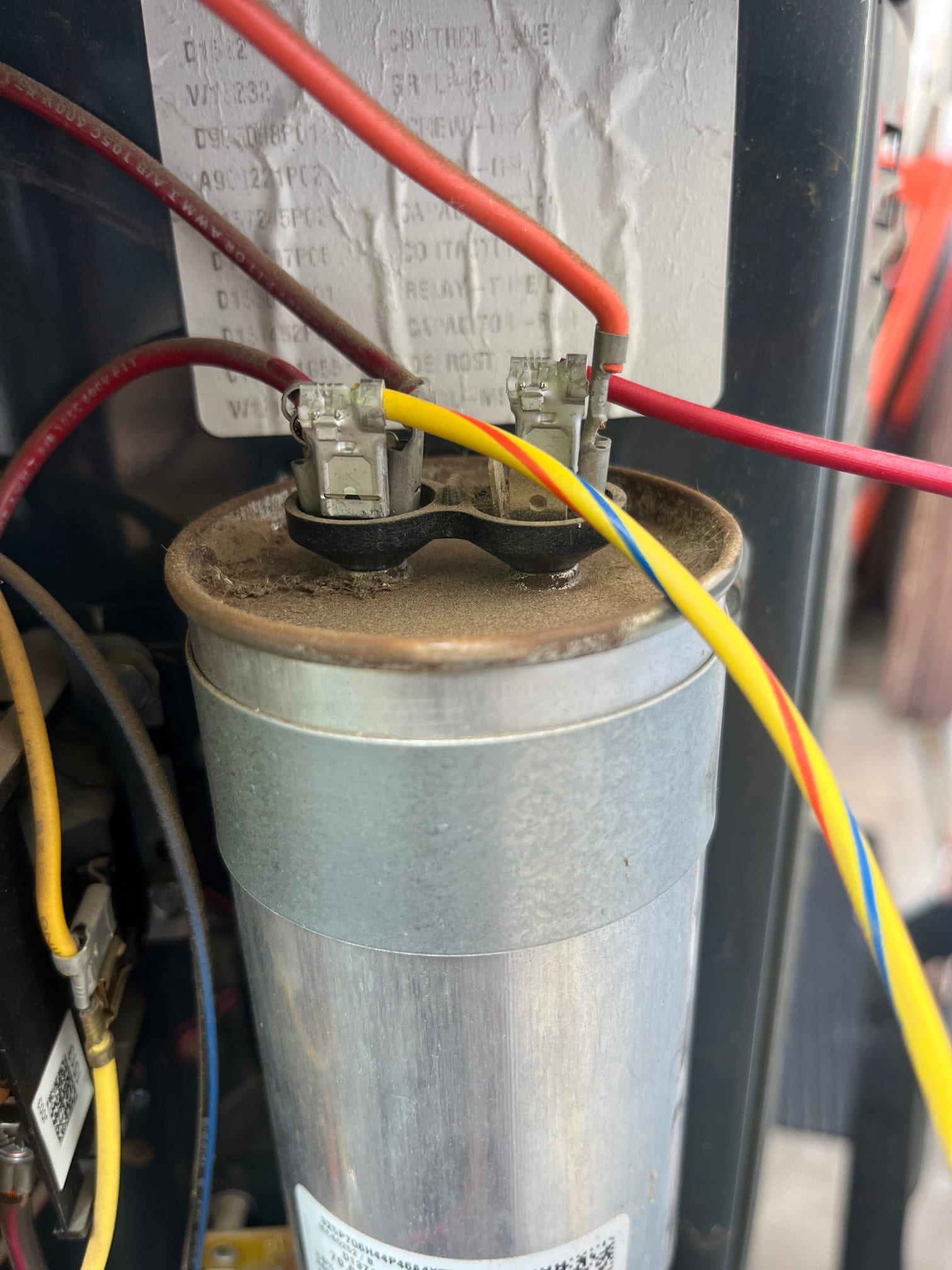 Dual-run capacitor installed in outdoor condenser, with red, yellow, and blue wires connected to clearly labeled terminals.