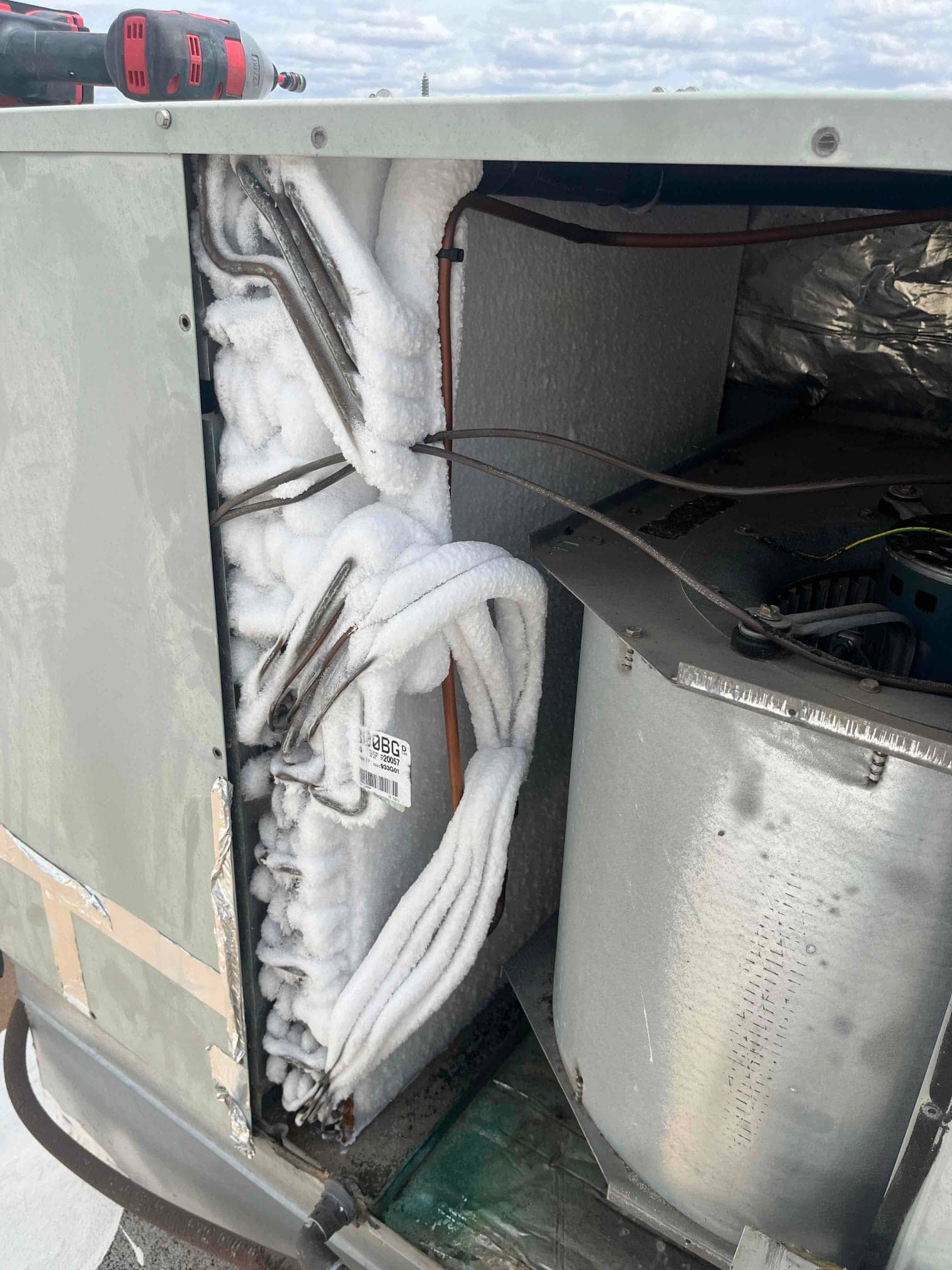 Evaporator coil and refrigerant lines heavily frosted inside an air handler cabinet, with blower housing visible next to the iced components.