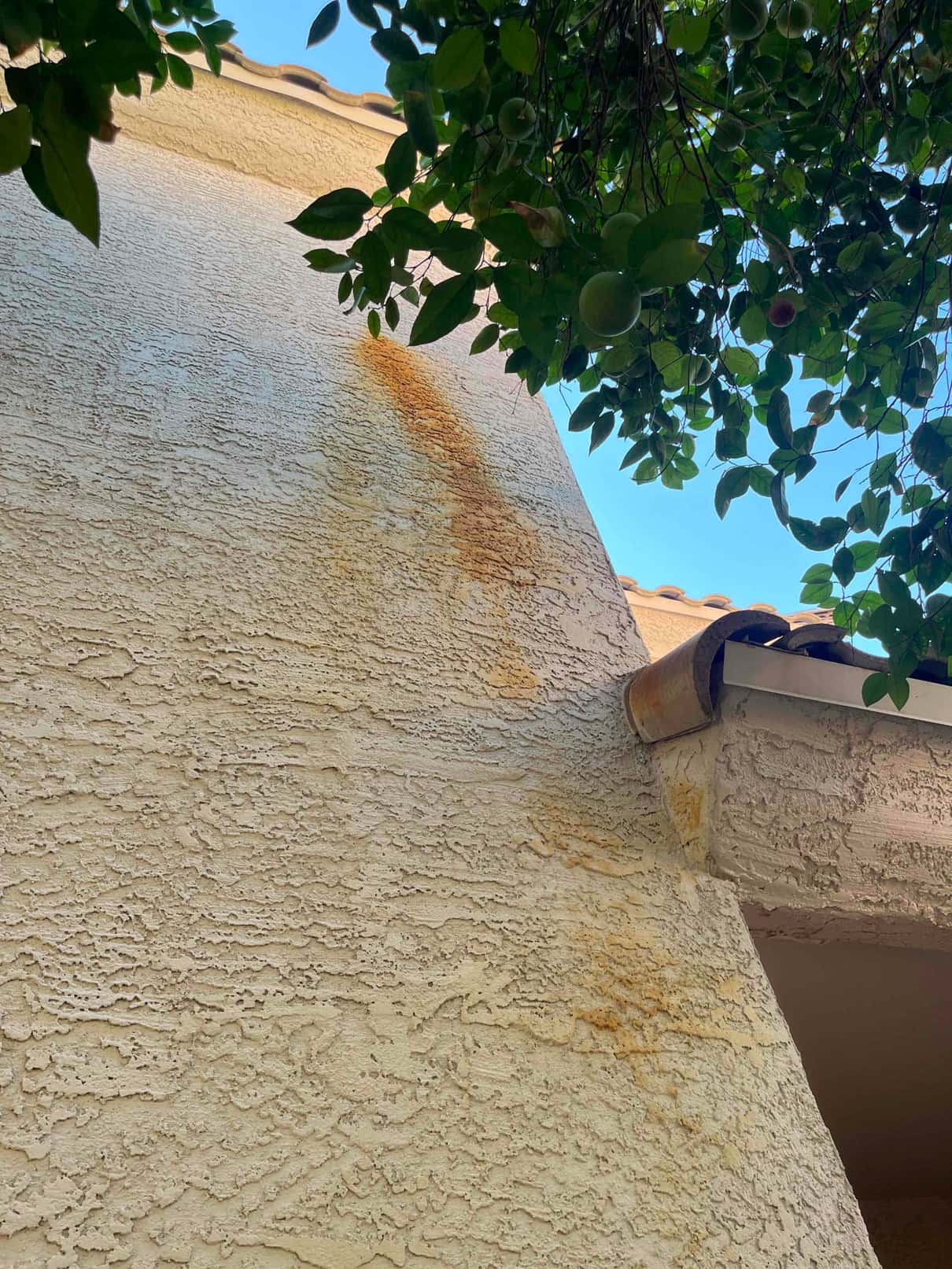 Exterior stucco wall under roof eave shows rust-colored staining below a drain outlet near the gutter.