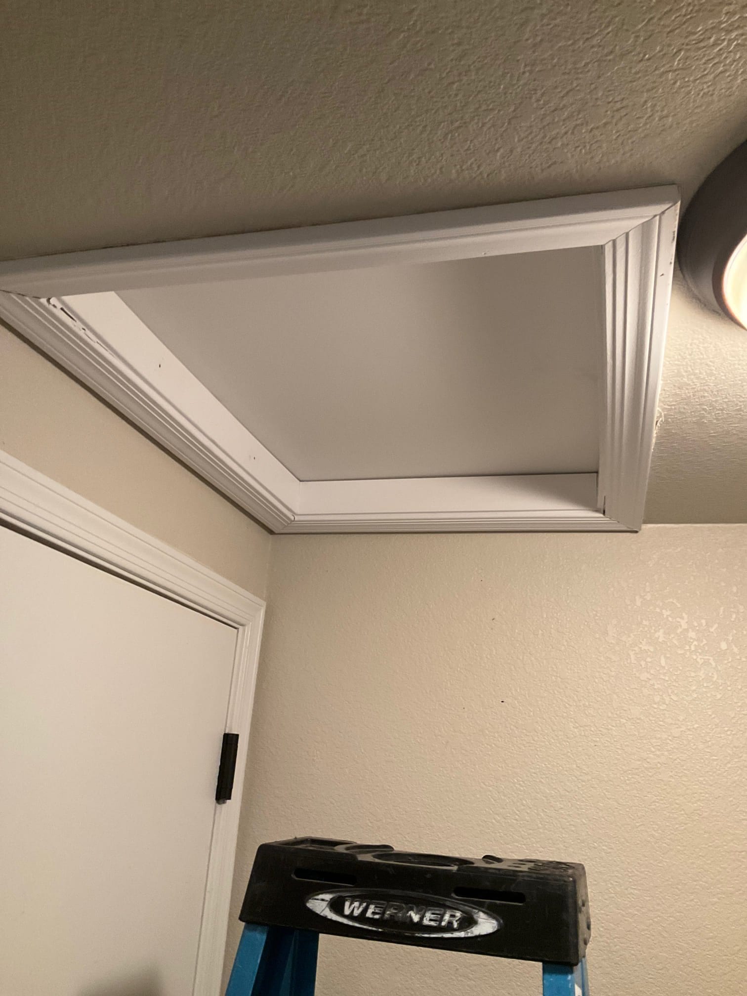 Finished attic access with trimmed return grille frame installed in the ceiling above a ladder, showing clean workmanship at the entry point.