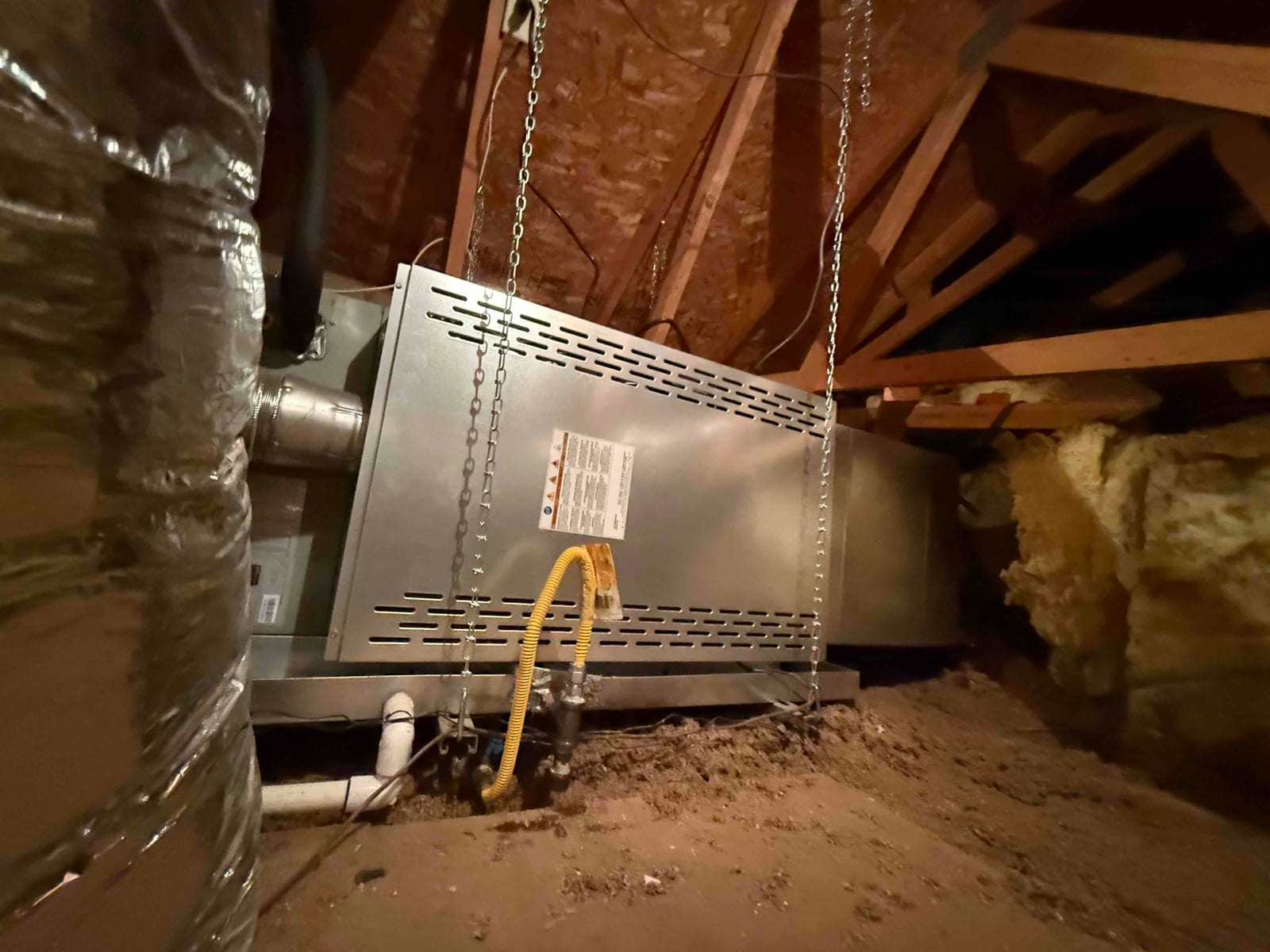 Horizontal attic air handler suspended with chains, connected to ductwork, condensate drain, and flexible gas line, showing completed installation.