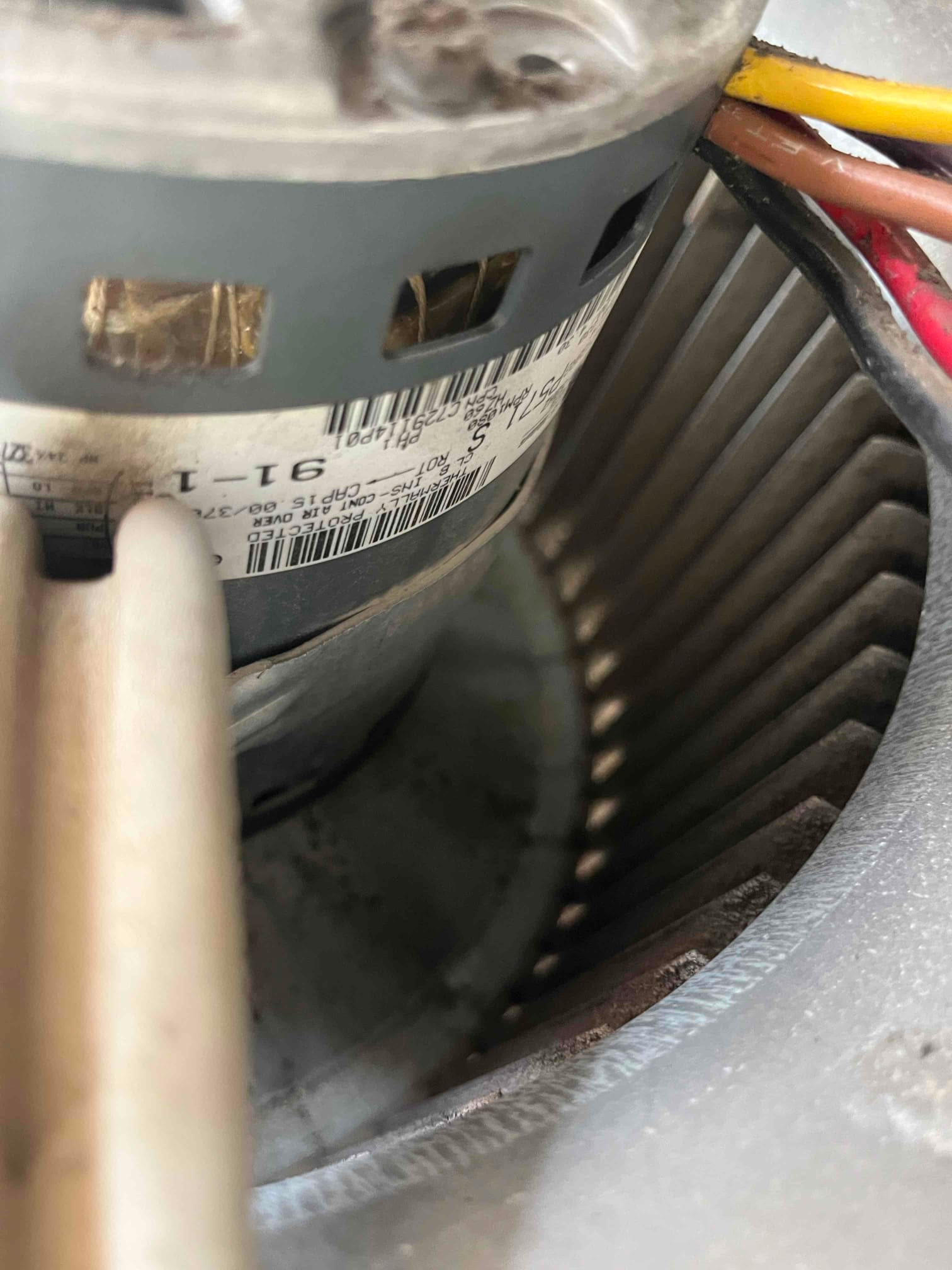 Indoor blower wheel and motor housing visible inside the air handler, showing wiring harness and vent openings on the motor.