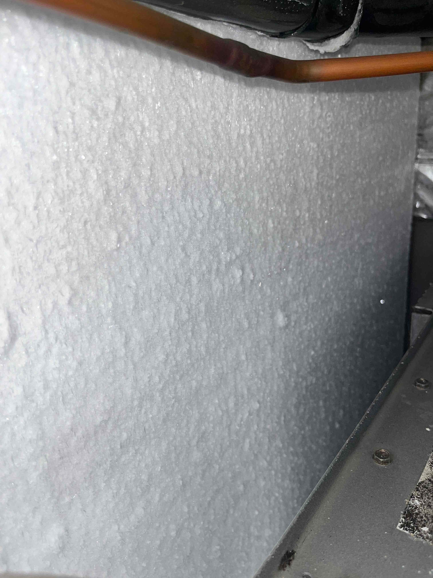 Indoor evaporator coil panel heavily frosted with ice buildup, visible adjacent refrigerant lines and air handler cabinet.