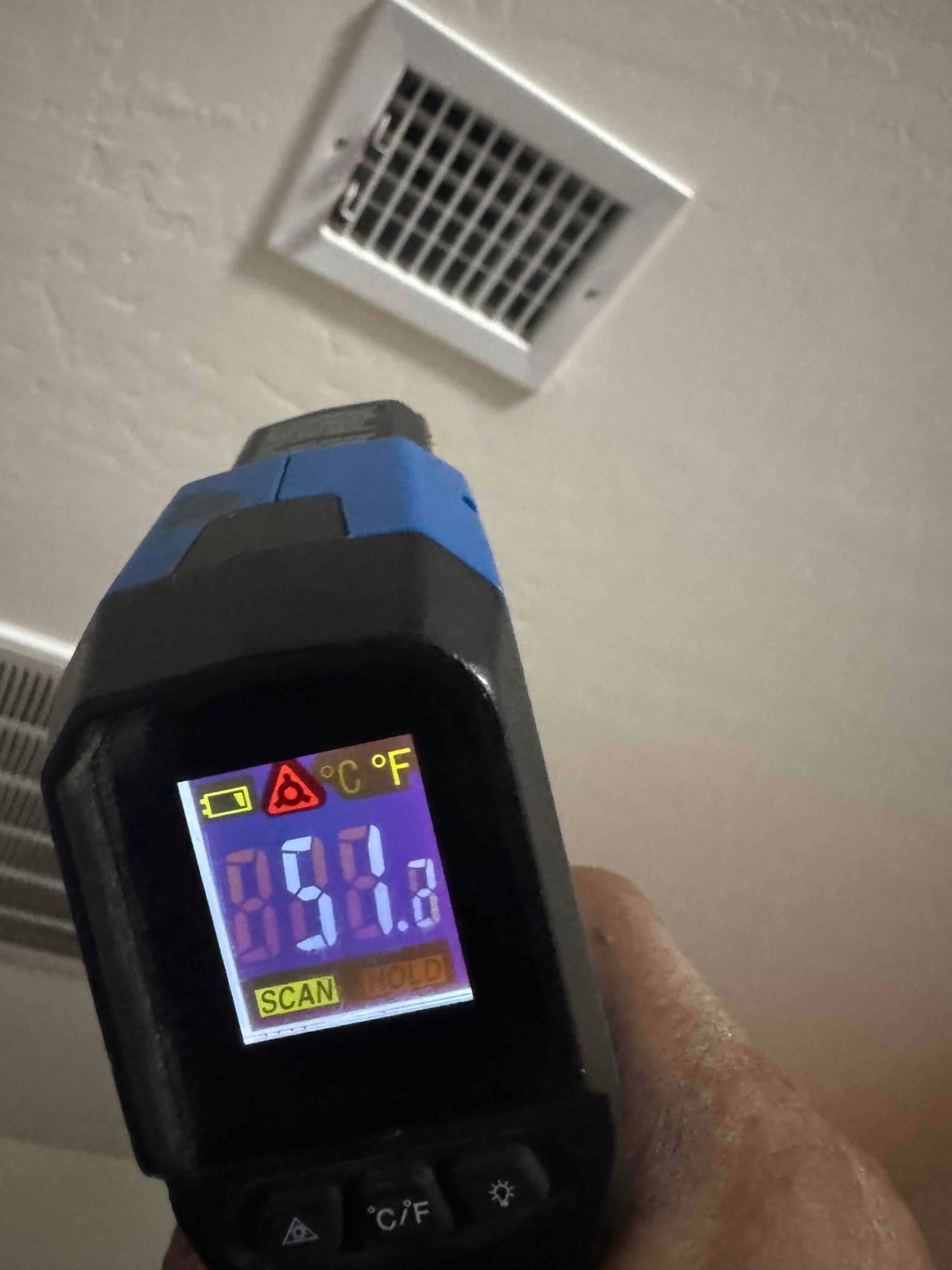 Infrared thermometer aimed at a ceiling supply register shows 58.8 degrees Fahrenheit during cooling airflow verification.