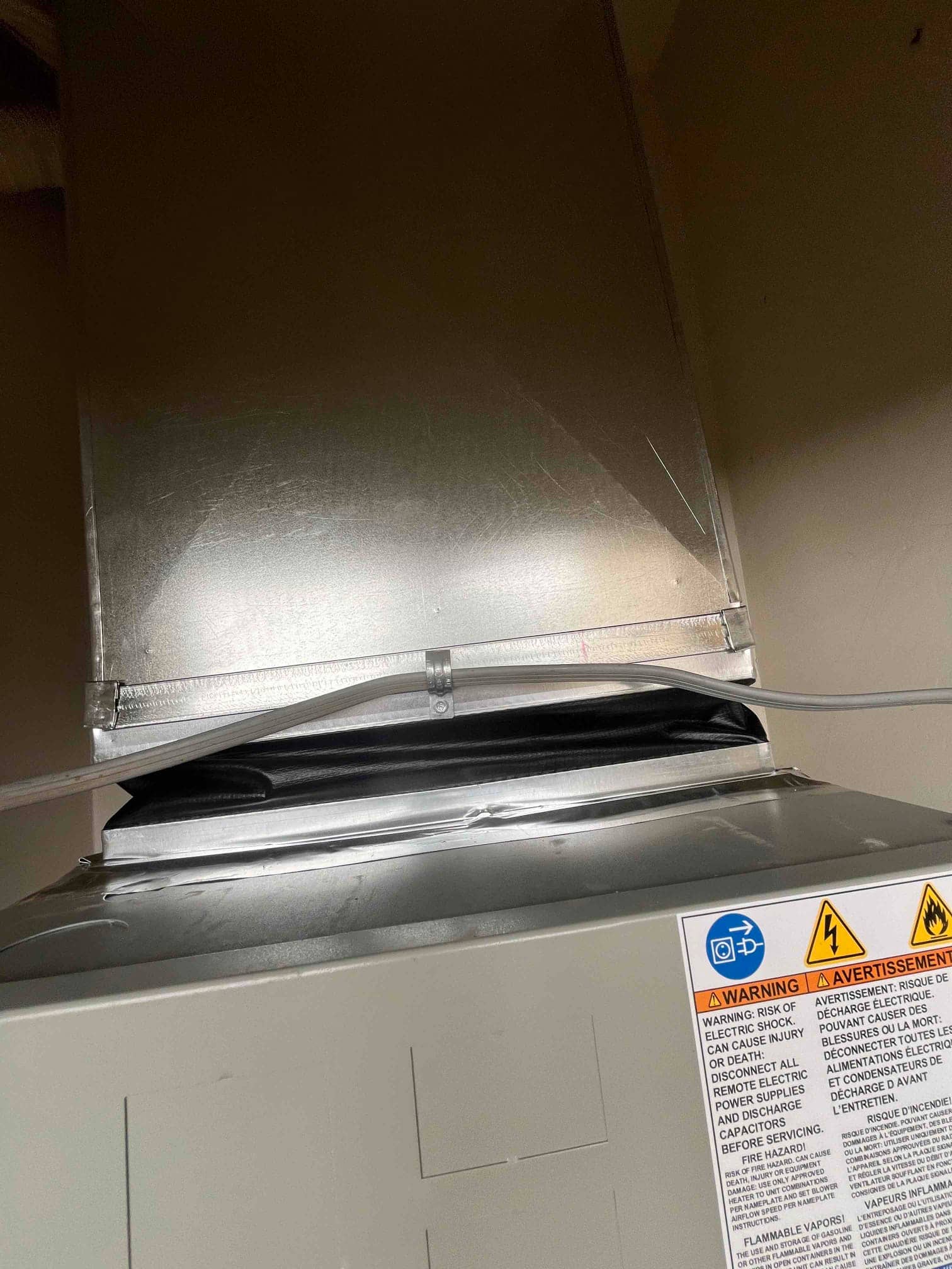 New air handler connected to a sealed sheet metal supply plenum with mastic and strapping, showing clean duct transition.