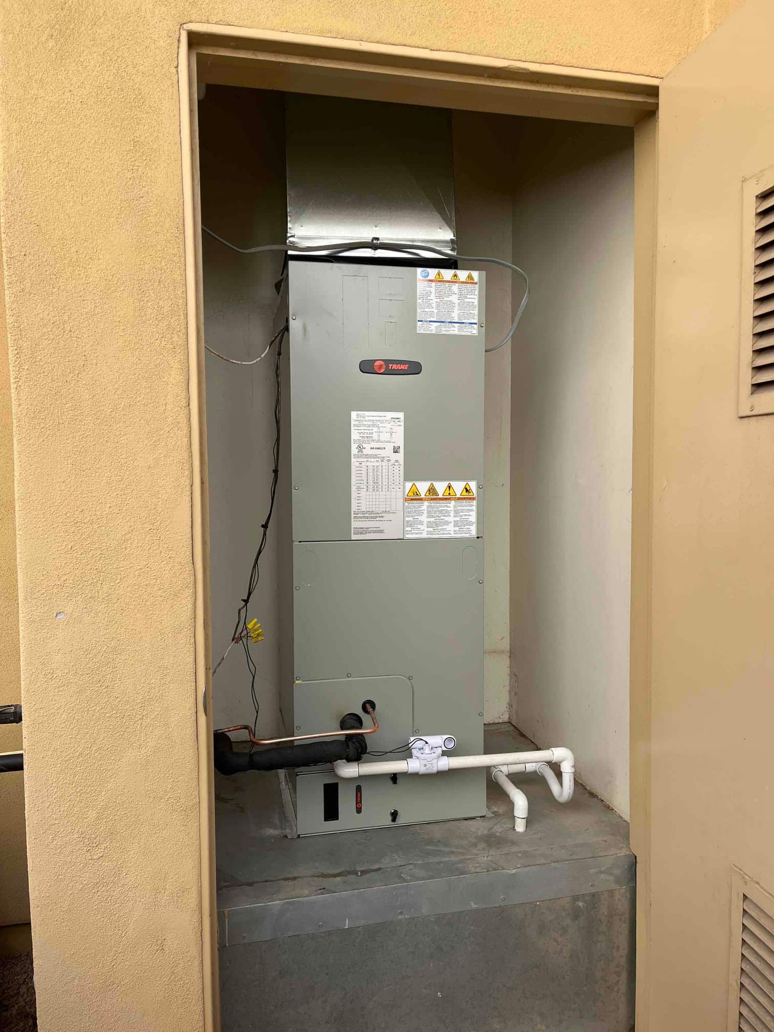 New air handler installed in a dedicated closet with insulated refrigerant lines, sheet metal plenum, and PVC condensate drain with cleanout.